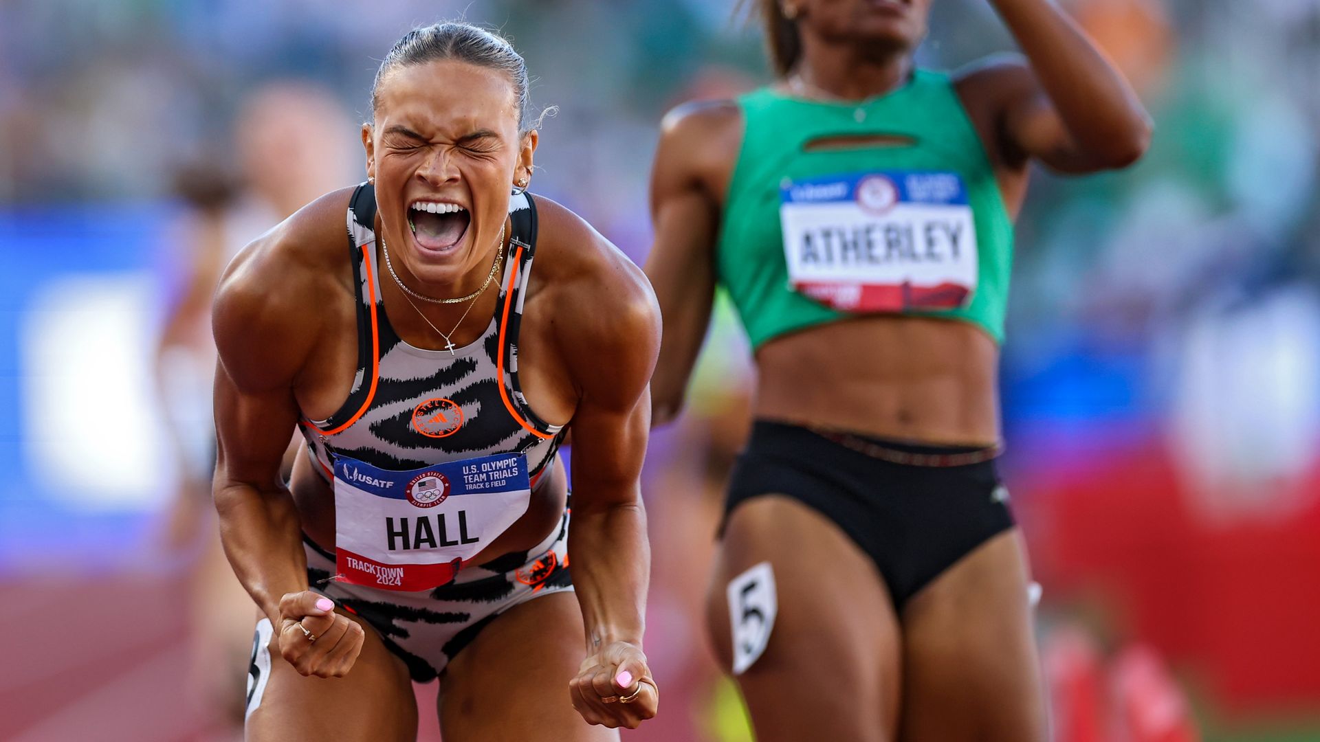 A woman celebrates with a yell after winning a race, with her hands clenched into fists. 
