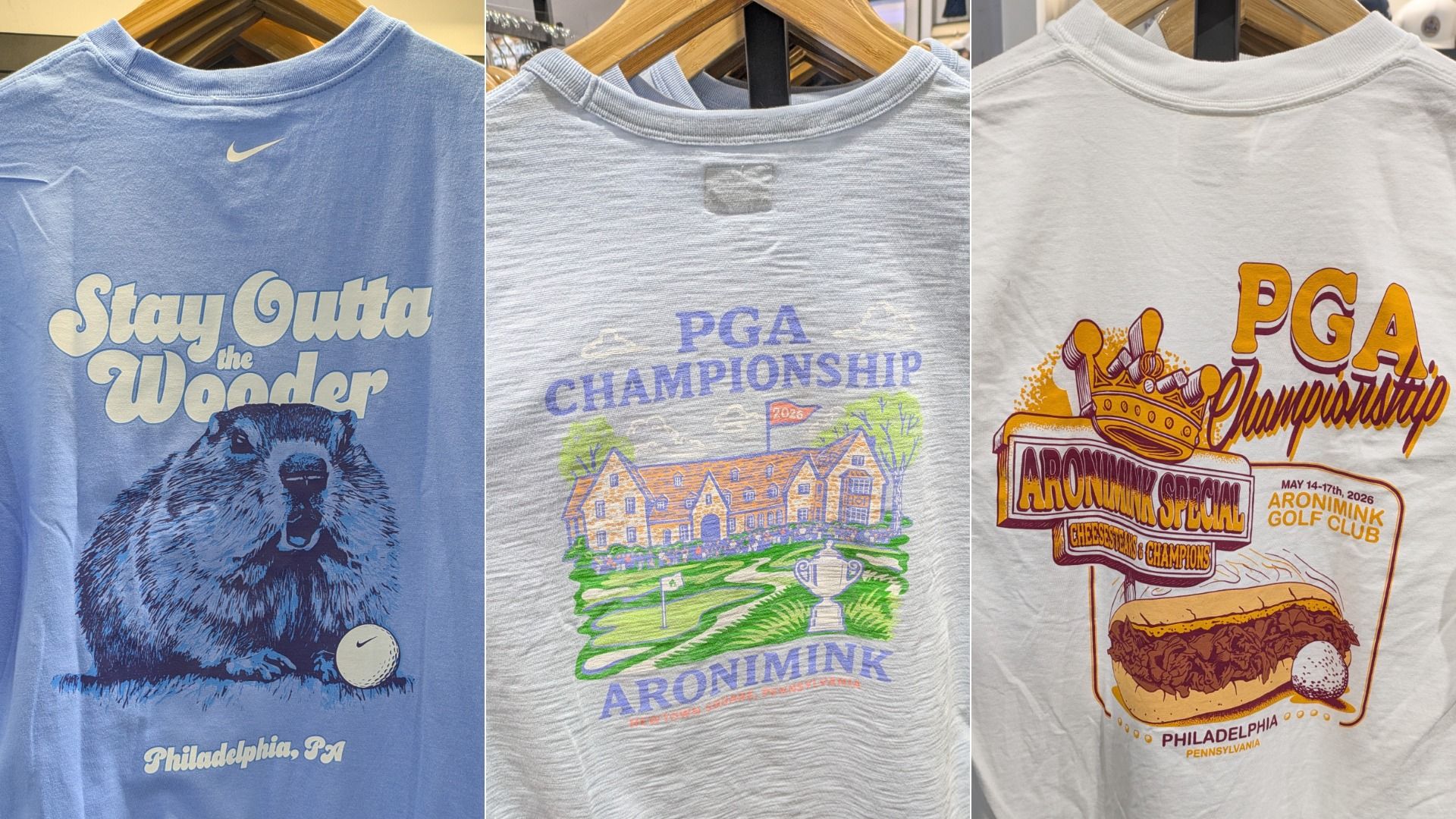 Three graphic T-shirts on hangers: left blue with Stay Gutta the Wooder and a beaver; middle gray PGA Championship golf course scene; right white with PGA Championship and crown burger image.