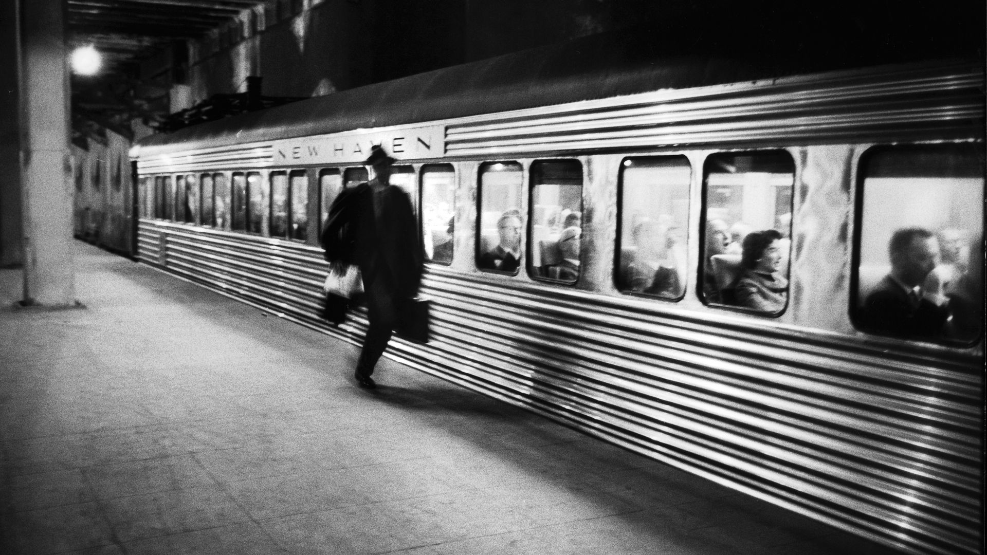 Silhouette of a man running against a silver train in a black and white photo