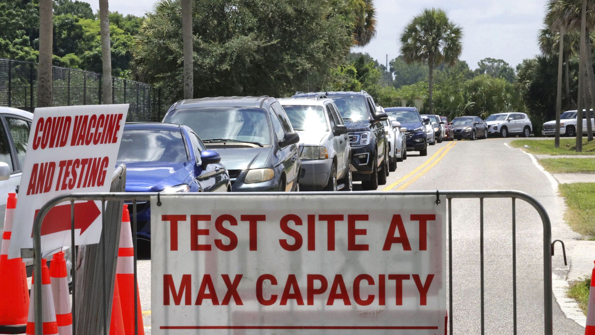 Picture of cars lining up for a testing site and a sign that reads "Test site at max capacity"