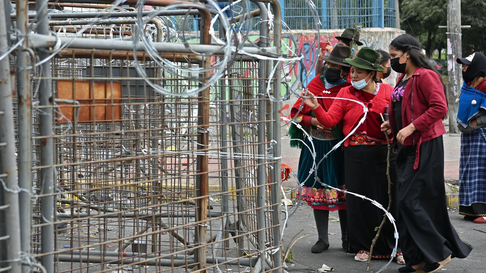 Indigenous Ecuadorian women stand outside barbed wire 