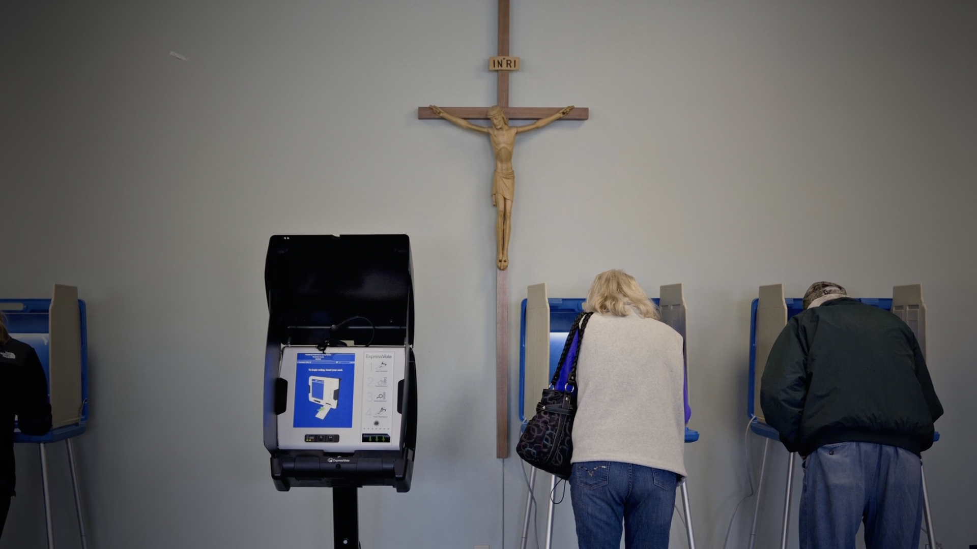 Voters cast ballots while a Cross on a wall towers over them.