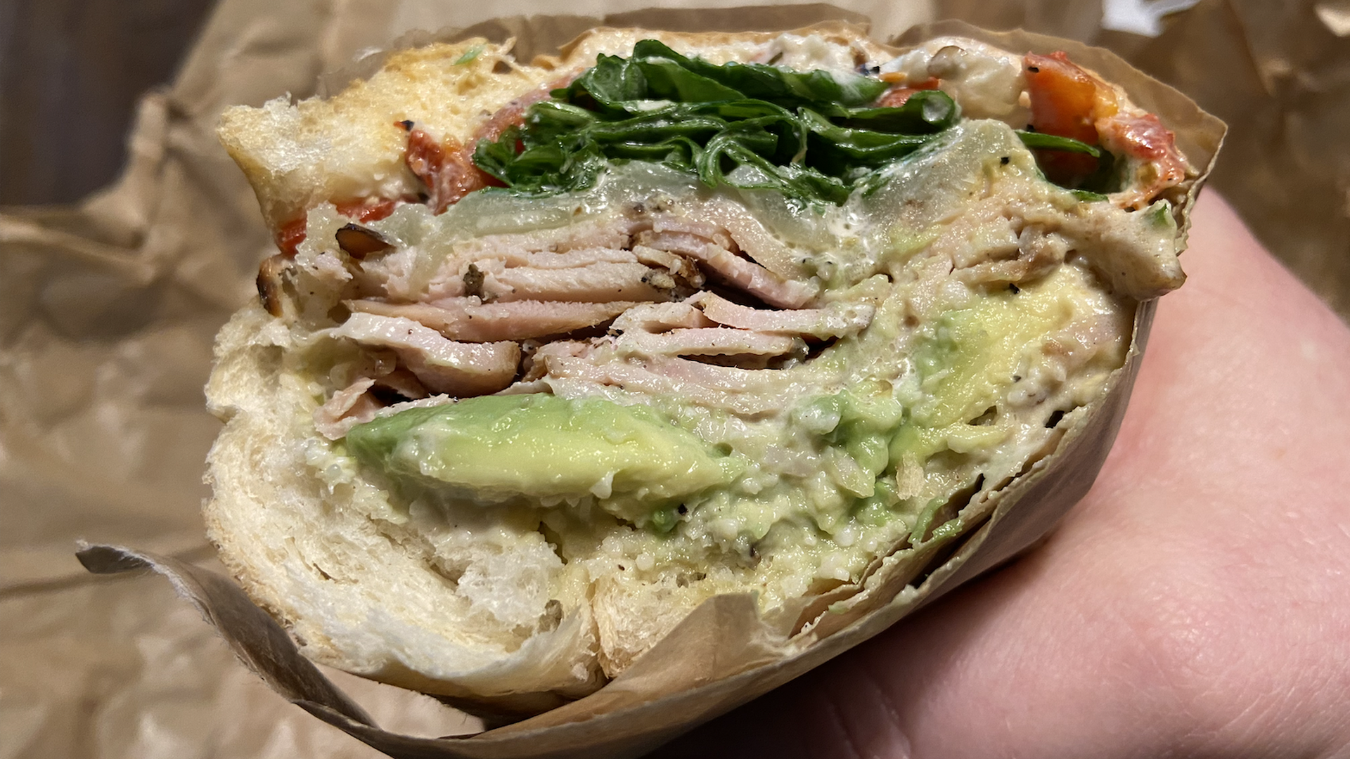 A hand holds a turkey subway sandwich bursting with sliced meat, avocado and parmesan peppercorn dressing
