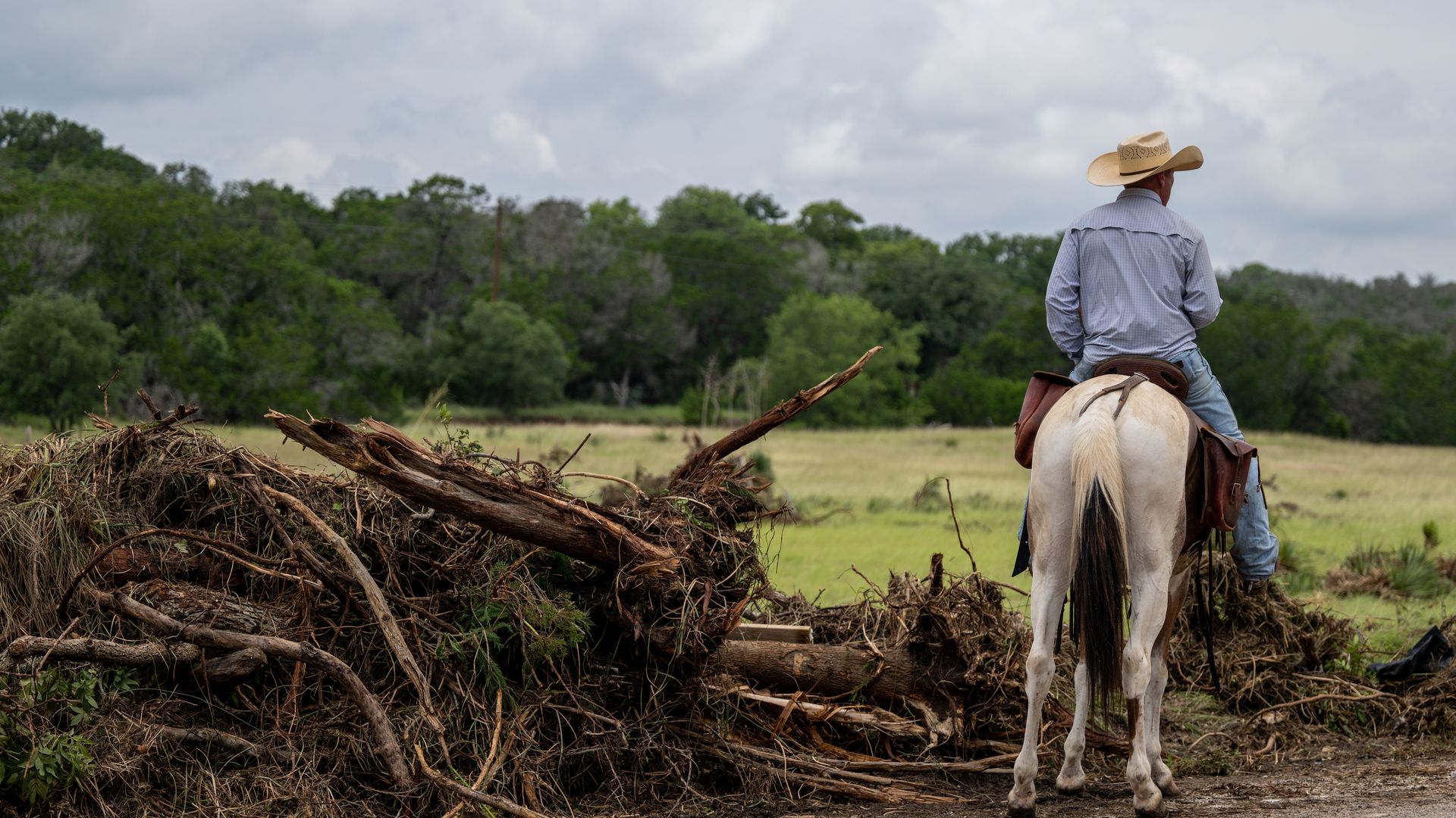 A man riding a white horse looks away from the camera into a field, surrounded by debris.
