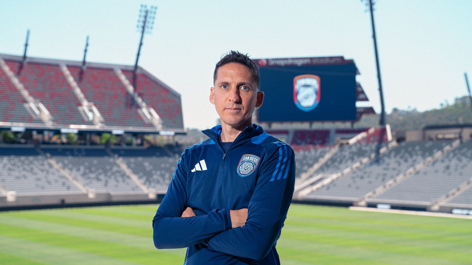 New San Diego FC head coach Mikey Varas stands in front of the field at Snapdragon Stadium.