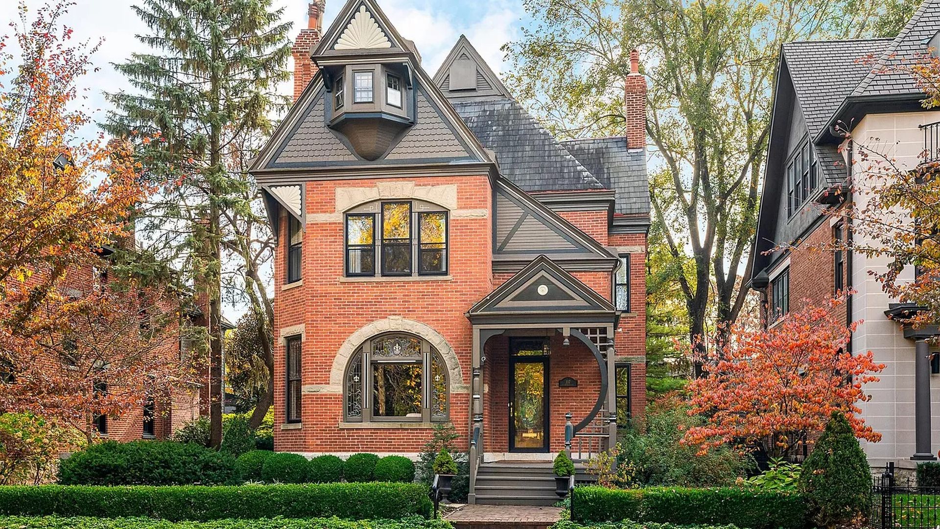 A multi-story brick home surrounded by trees and bushes.