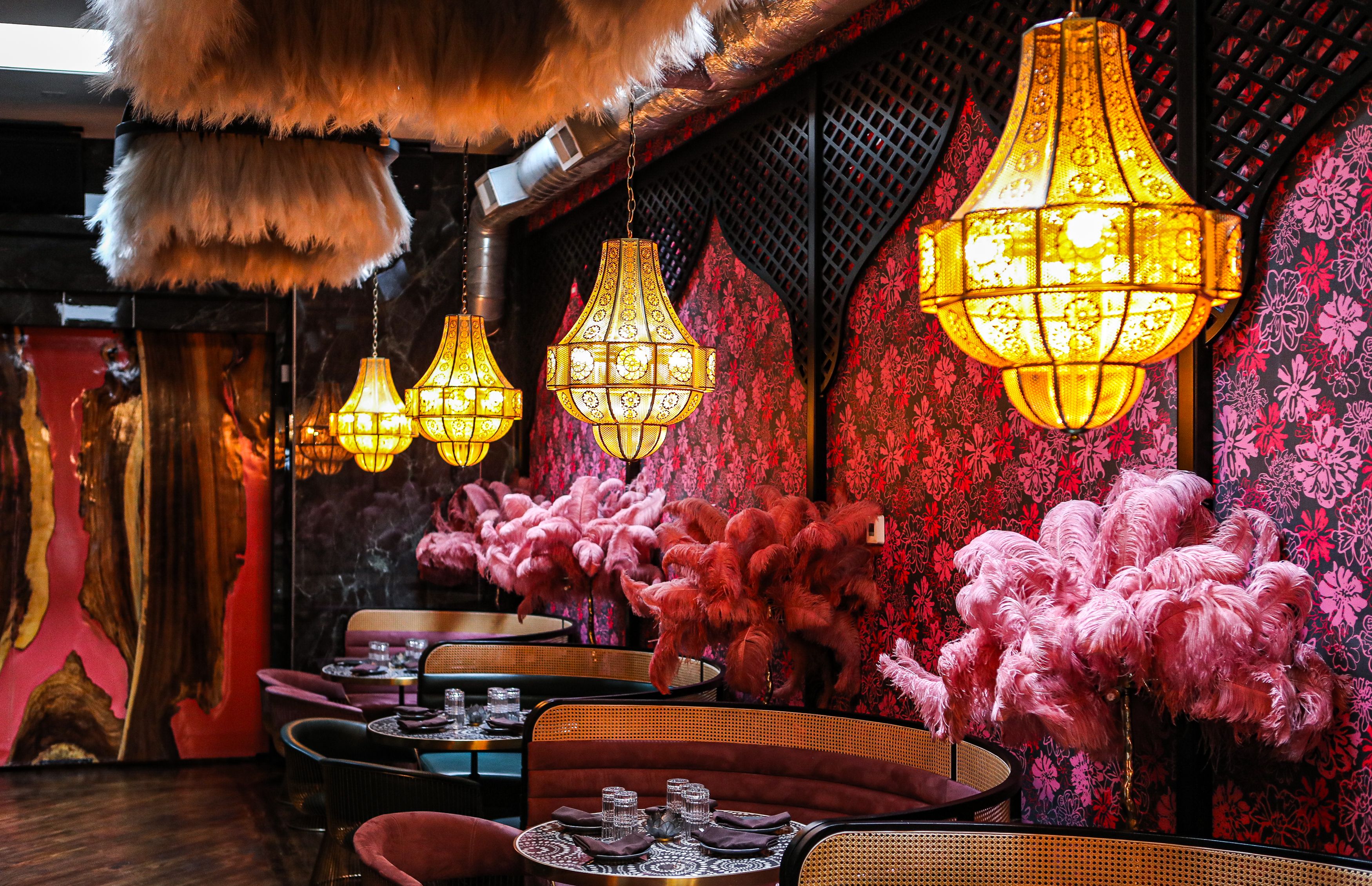 The interior of Mya by Medi, with planters full of pink feathers, pink and red wallpaper, large booths and chandeleirs.