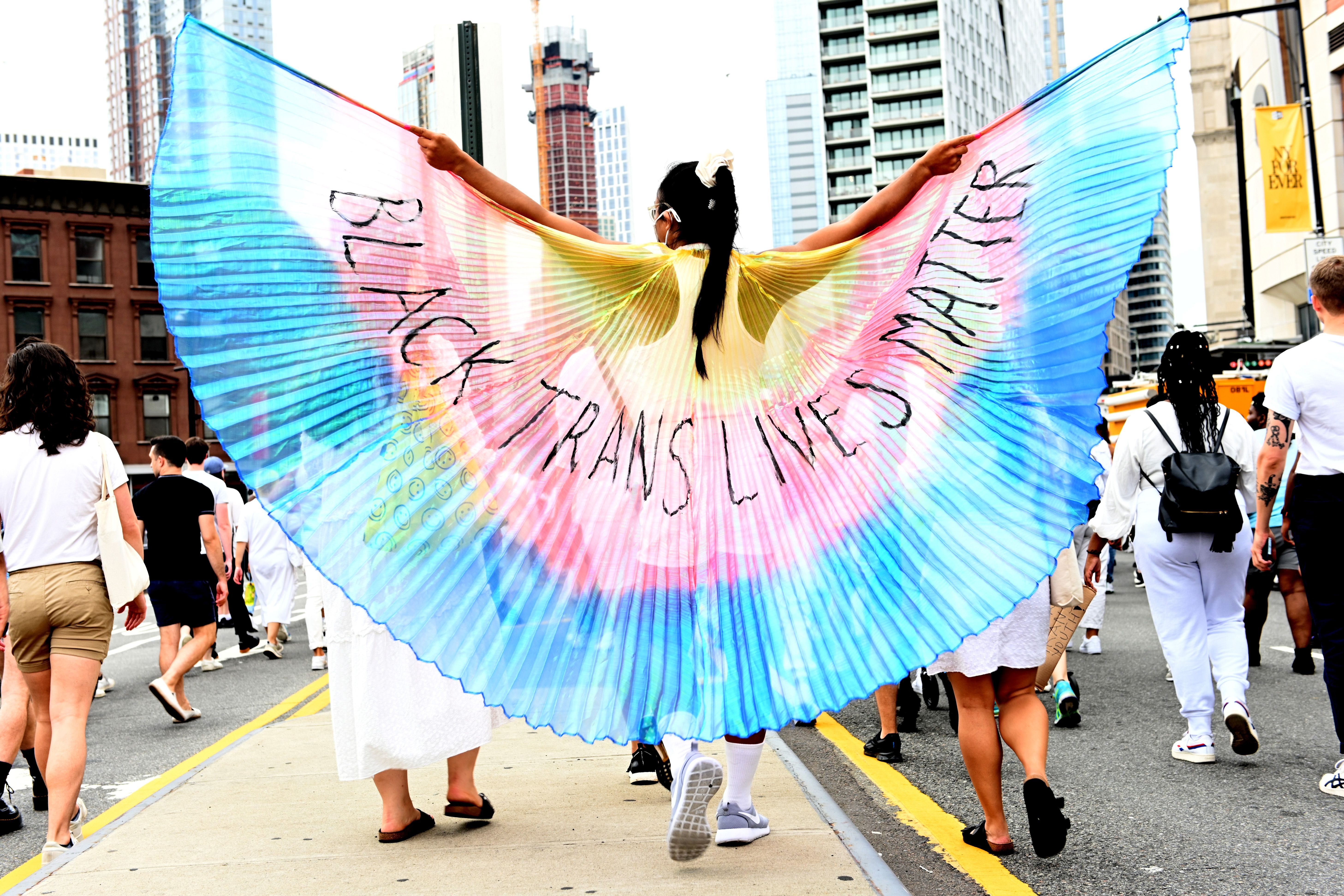 Photo of a person wearing wings in the colors of blue, pink and yellow with the words "Black Trans Lives Matter"