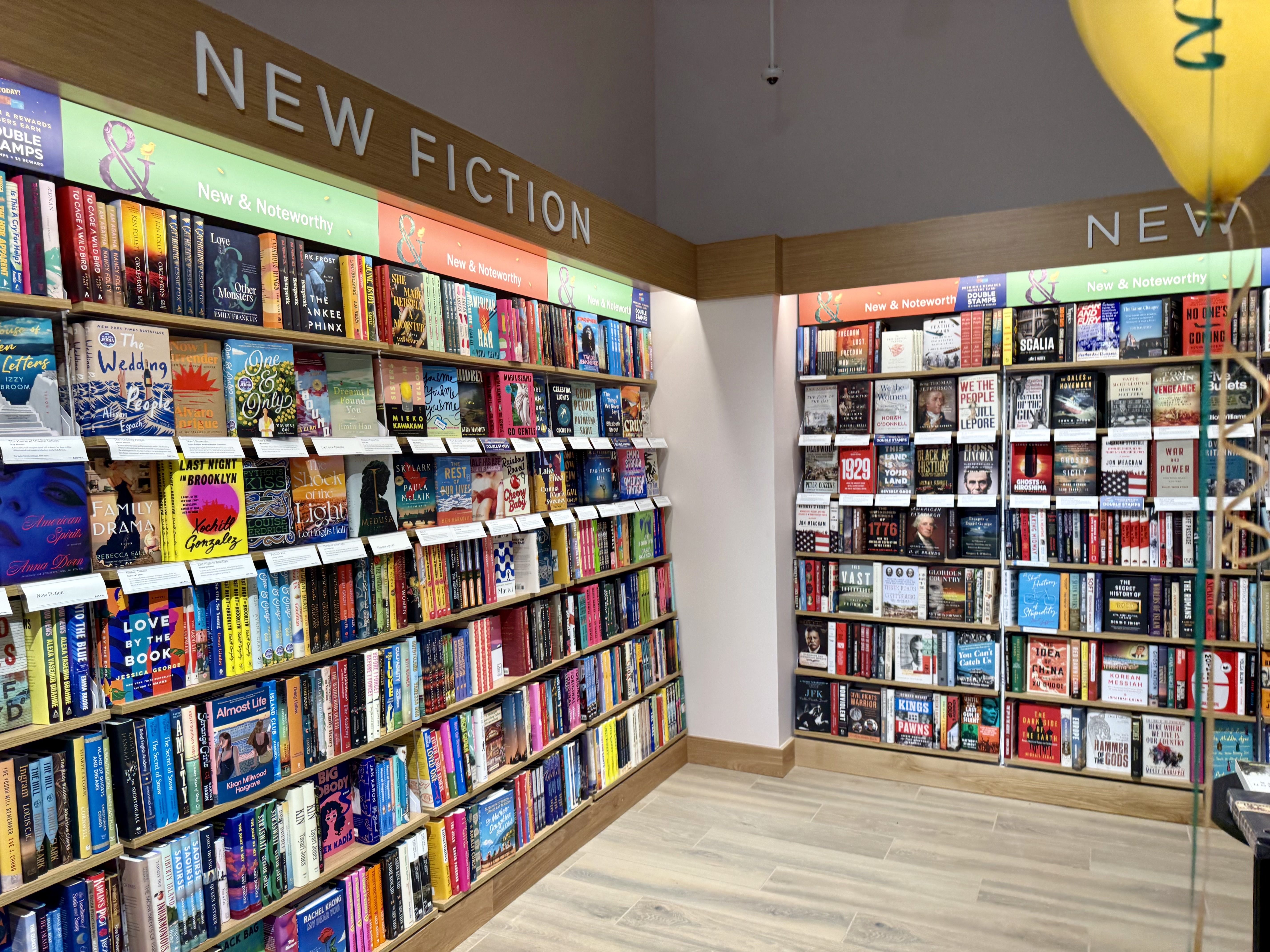 Interior of a Barnes & Noble bookstore with shelves of new fiction and nonfiction books displayed beneath large signs.