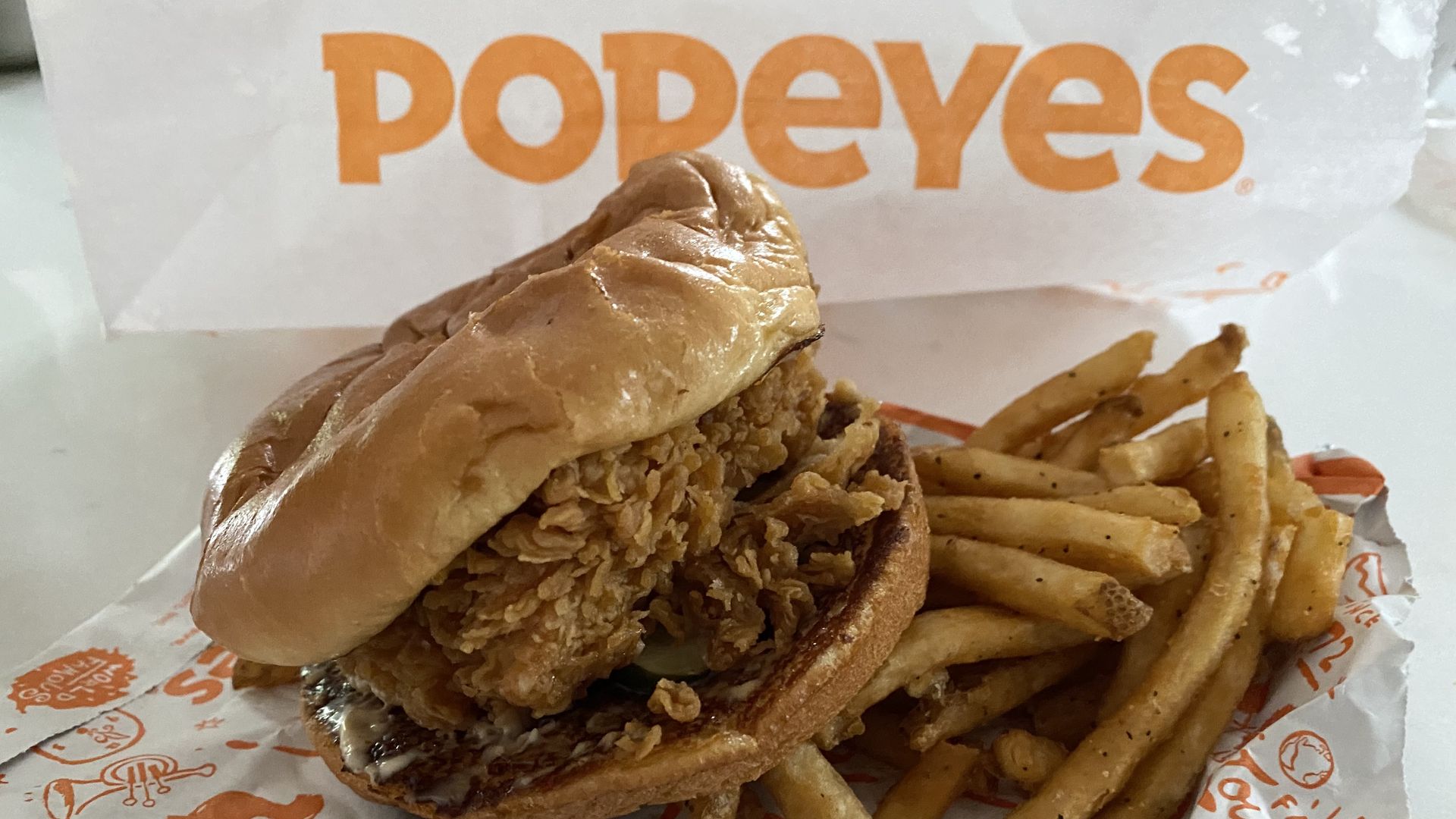 Popeyes chicken sandwich on fries with bag in background