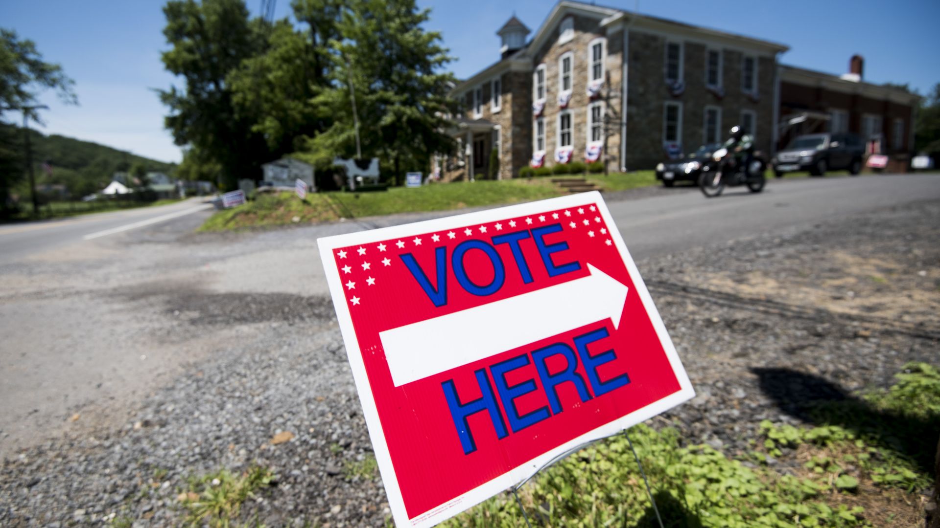 Vote here sign on a lawn pointing to a large building