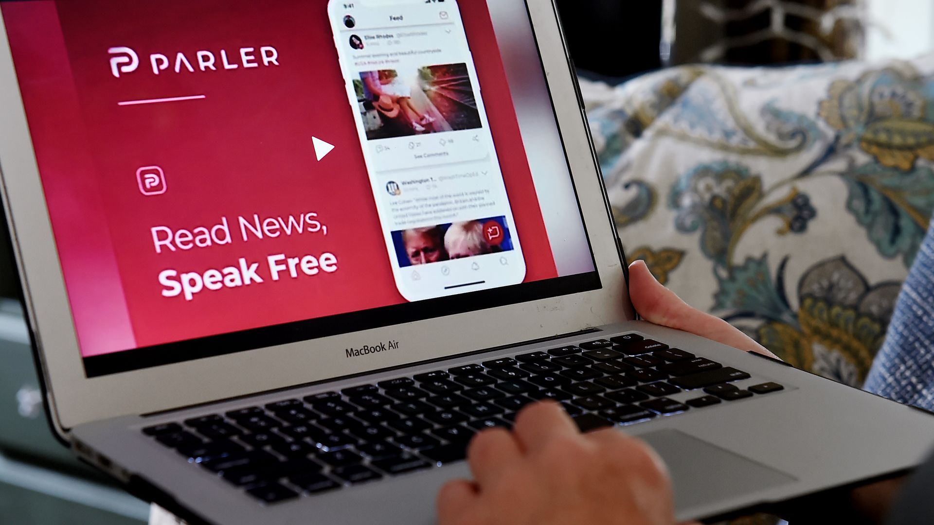 Photo of two hands holding up a laptop with a Parler ad on the screen