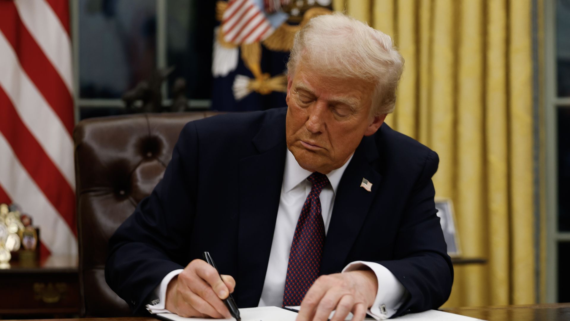 President Trump signs paperwork at his desk in the Oval Office.