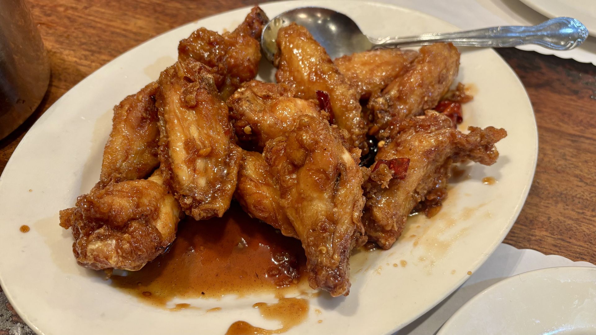 Plate of crispy fried chicken pieces in a glossy brown sauce, with red chili bits and sesame seeds, on a white plate with a spoon.
