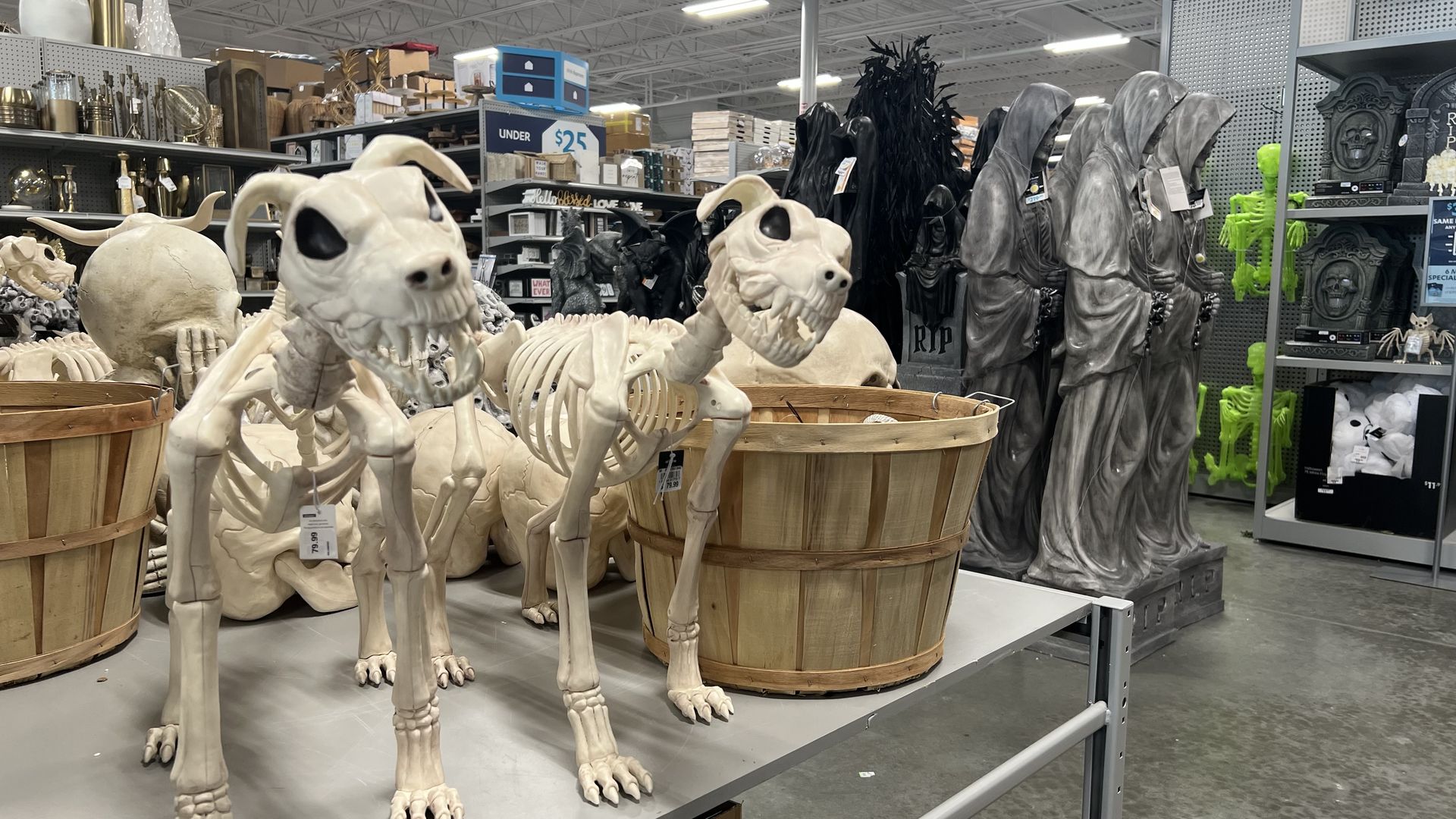 Store display of Halloween decorations featuring skeletal dogs, robed grim reaper figures, green skeletons, and other spooky items on shelves and tables.