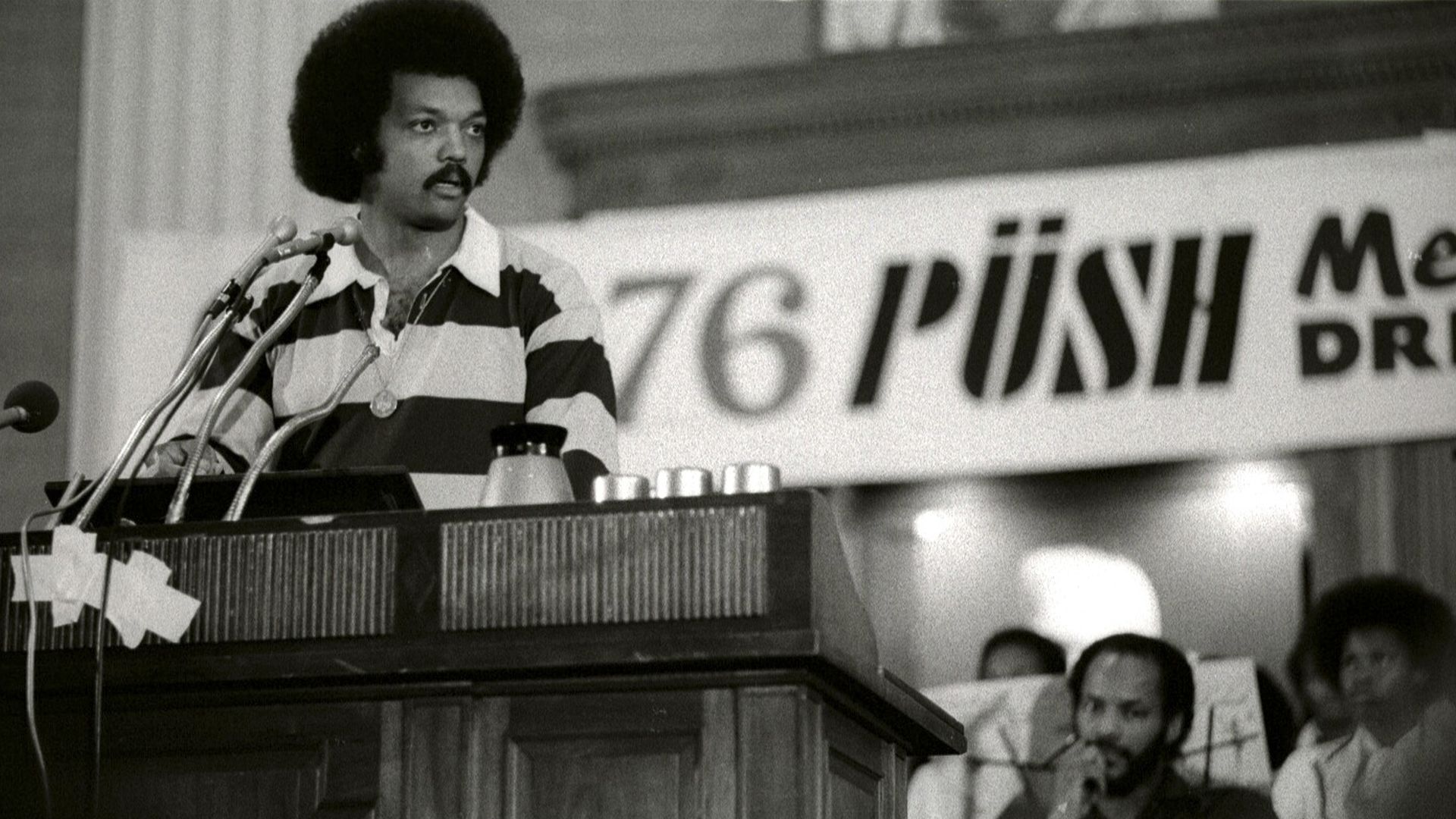 Jesse Jackson at a podium in front of sign that reads "76 PUSH"