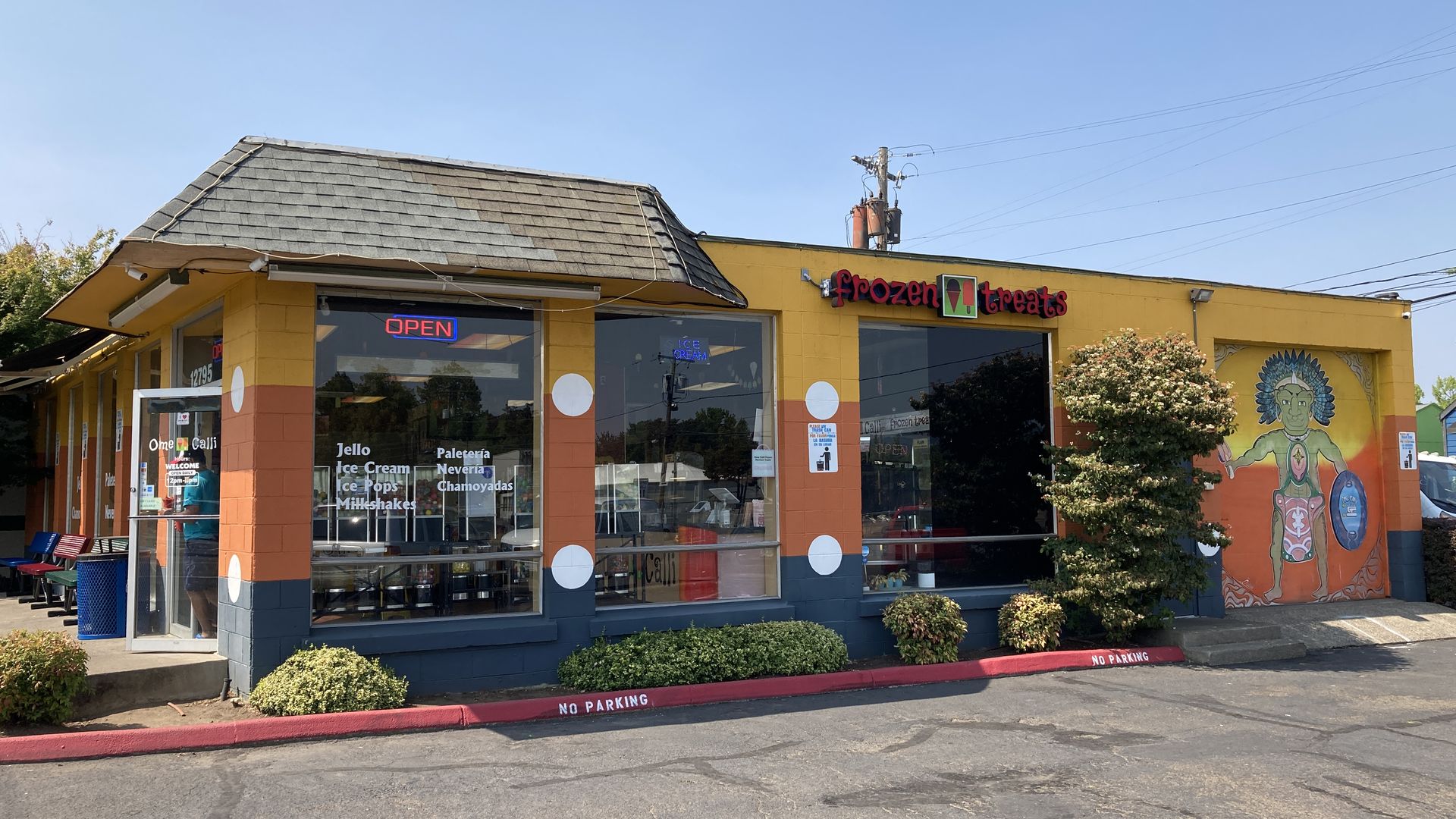 A colorful one-story building with a neon open sign flashing and a sign reading Frozen Treats.