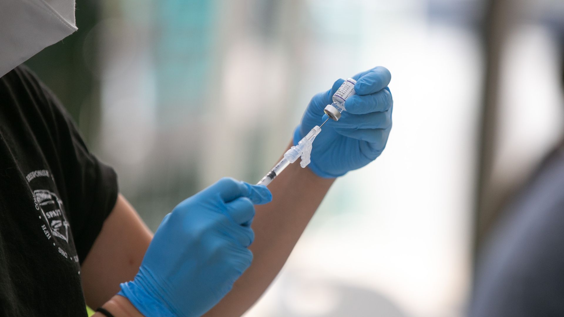 Photo of a medical worker holding up a COVID vaccine shot with gloved hands