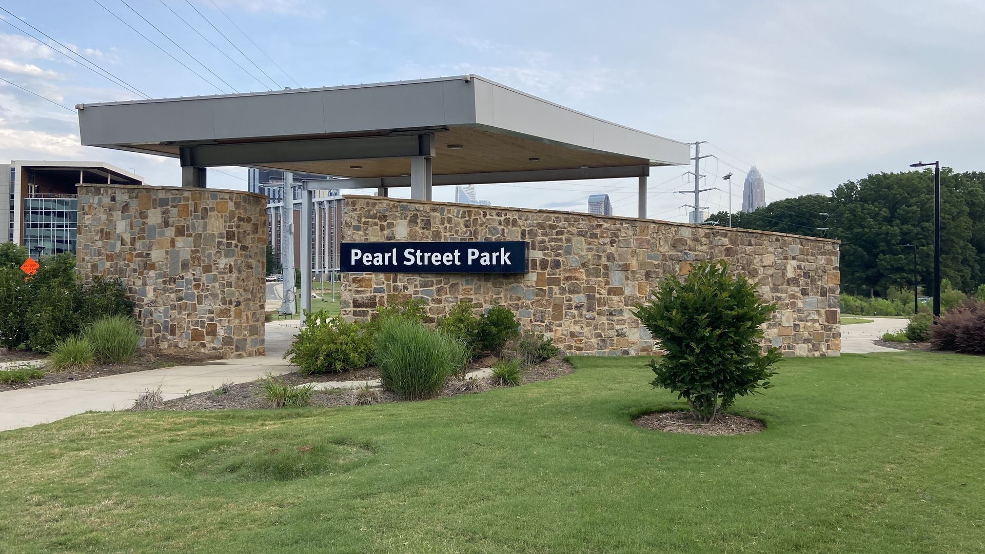 Pearl Street Park sign on a pavilion with the Charlotte skyline in the background. 