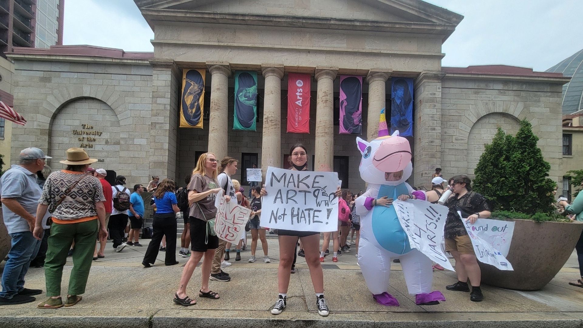 A protester holds a sign that says "Make Art Not Hate" outside of the University of the Arts.