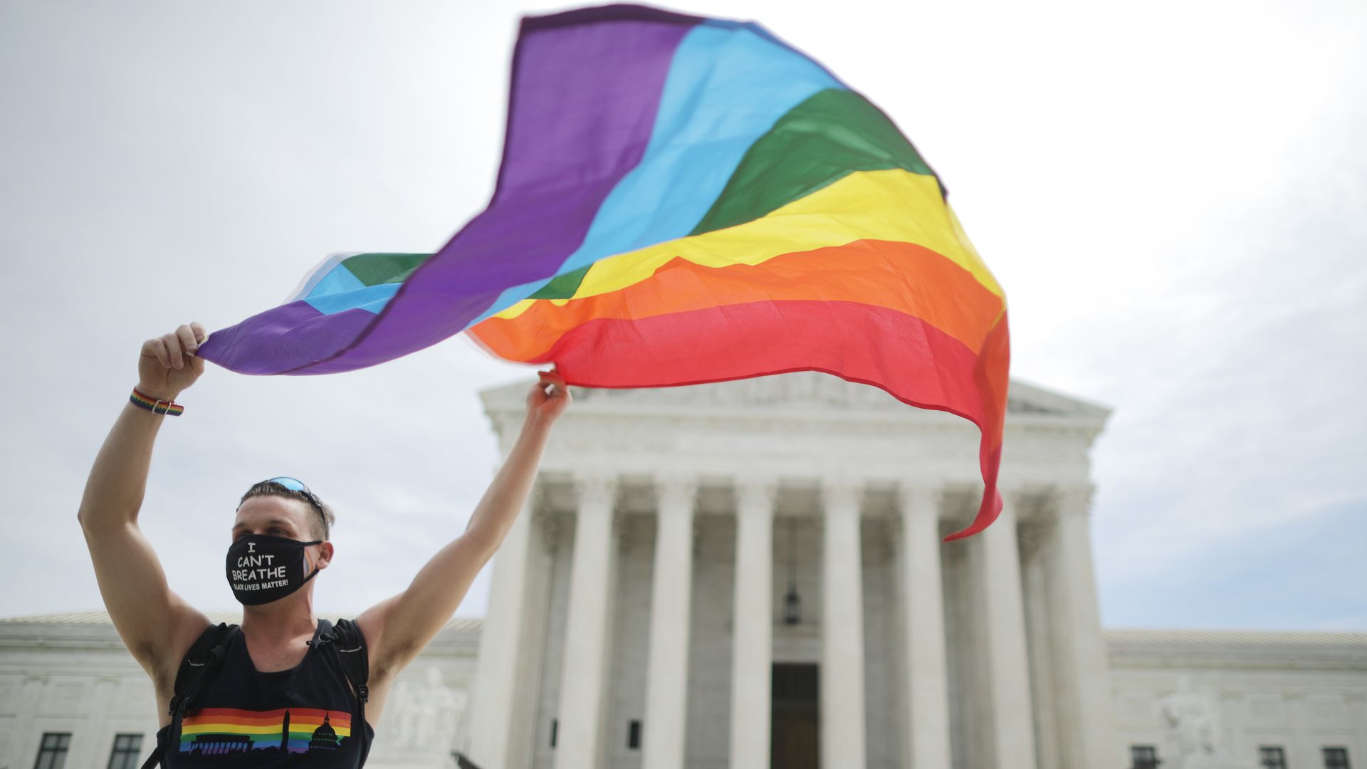 A person holding a pride flag in front of the Supreme Court building.