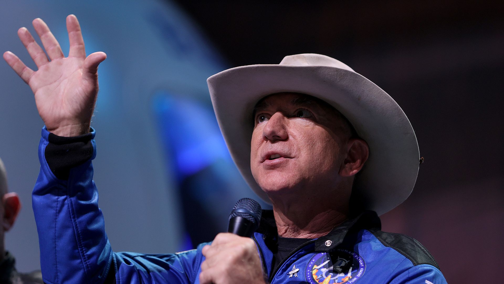 Jeff Bezos speaking and raising his hand at a Blue Origin event