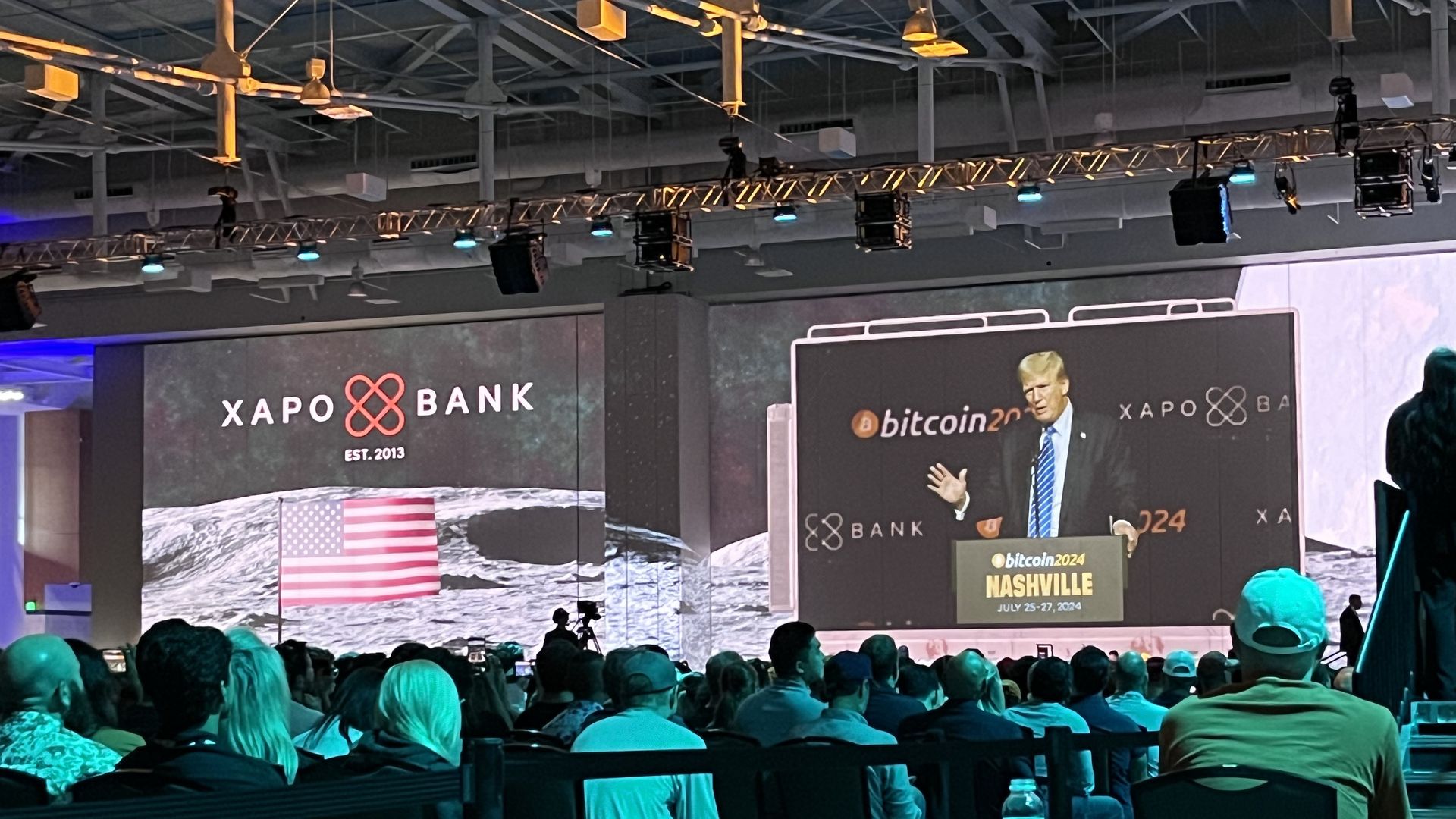 A photo of a speaker at a conference shown on a giant screen, with the words "Bitcoin2024" in the background. 