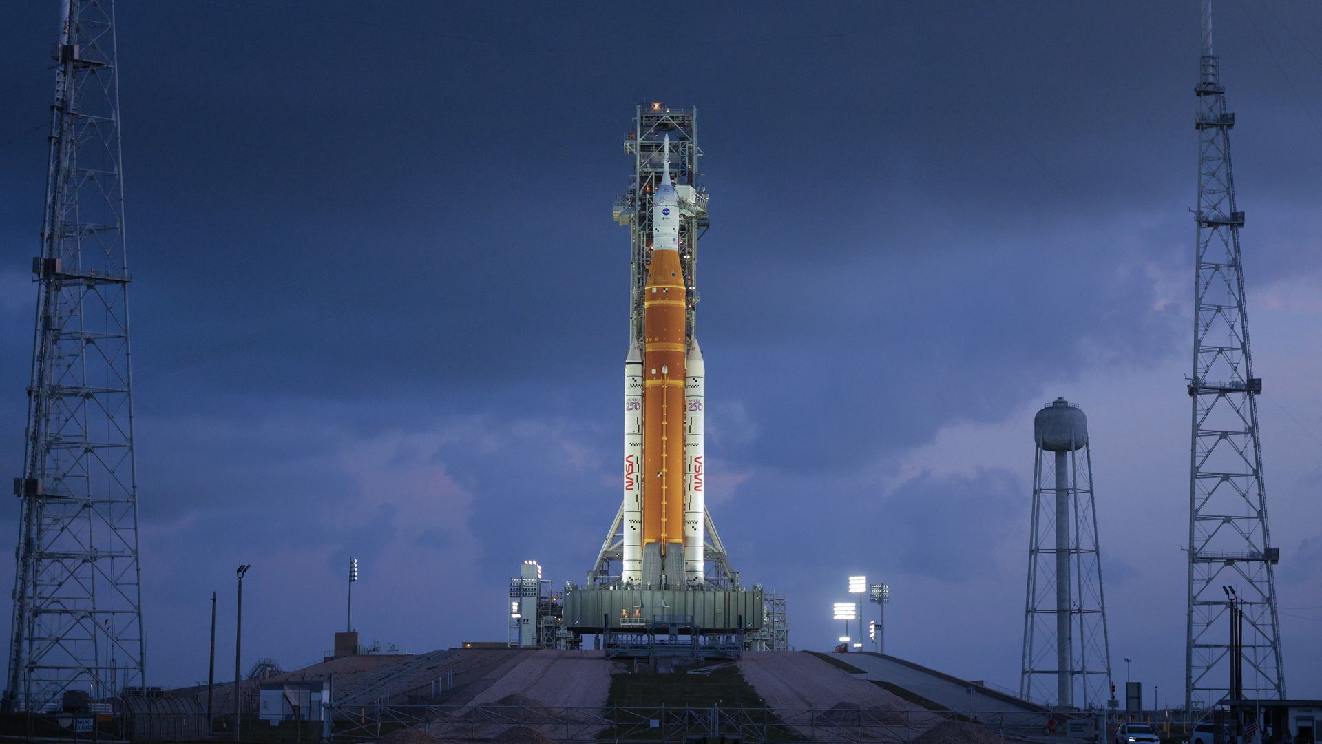 The Artemis II rocket sits on the launchpad, brightly lit against a night sky.