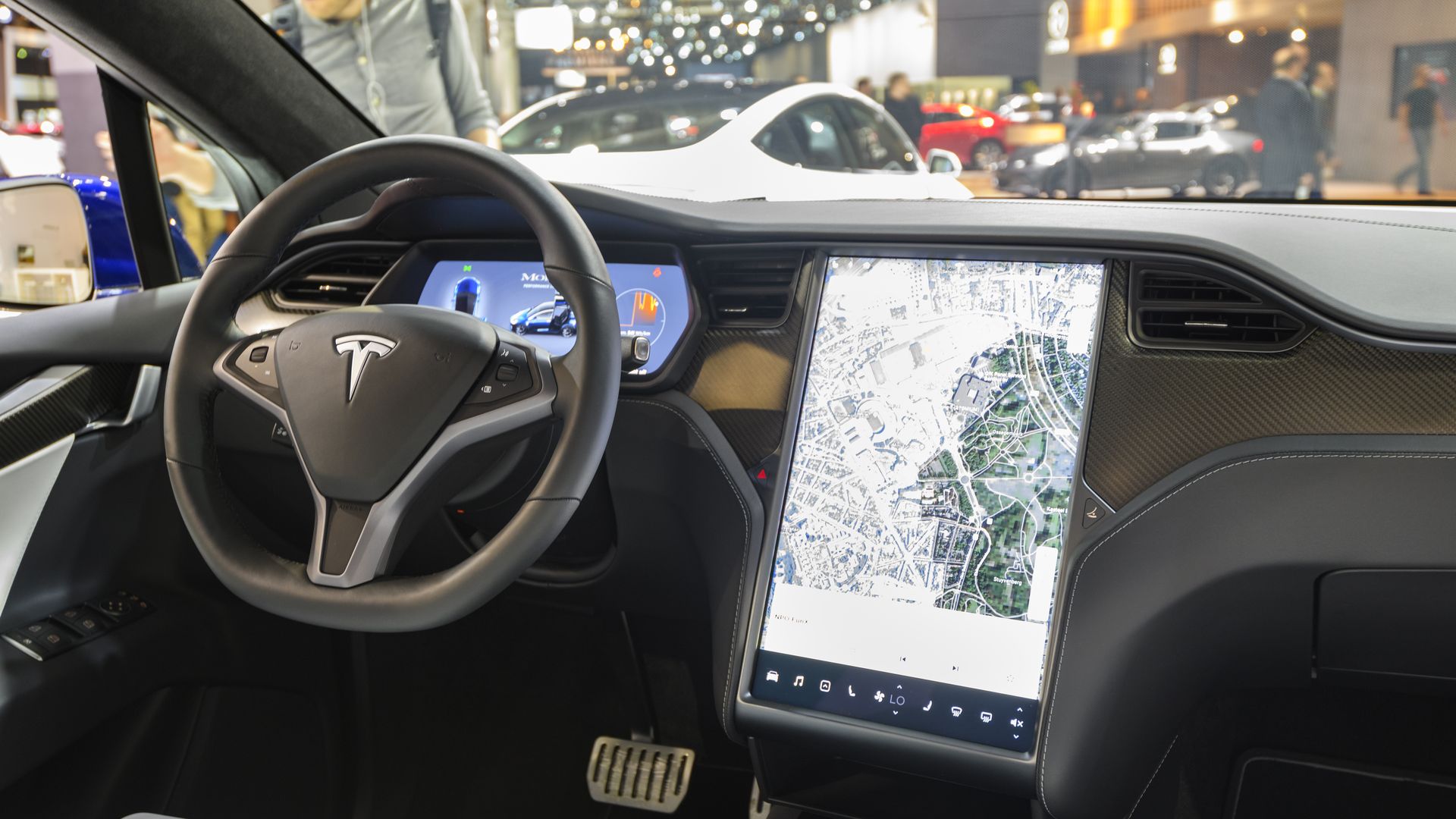 The interior of a Tesla vehicle showing a steering wheel and a large upright touchscreen