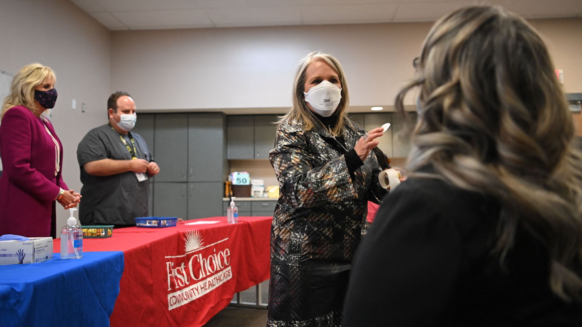 Photo of Michelle Lujan Grisham in a mask giving a sticker to a woman