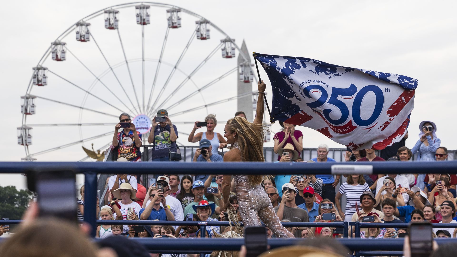 Crowd at a celebration watches a rodeo rider on a horse, waving a large blue, white, and red flag that reads 250th Anniversary; a giant Ferris wheel looms in the background.