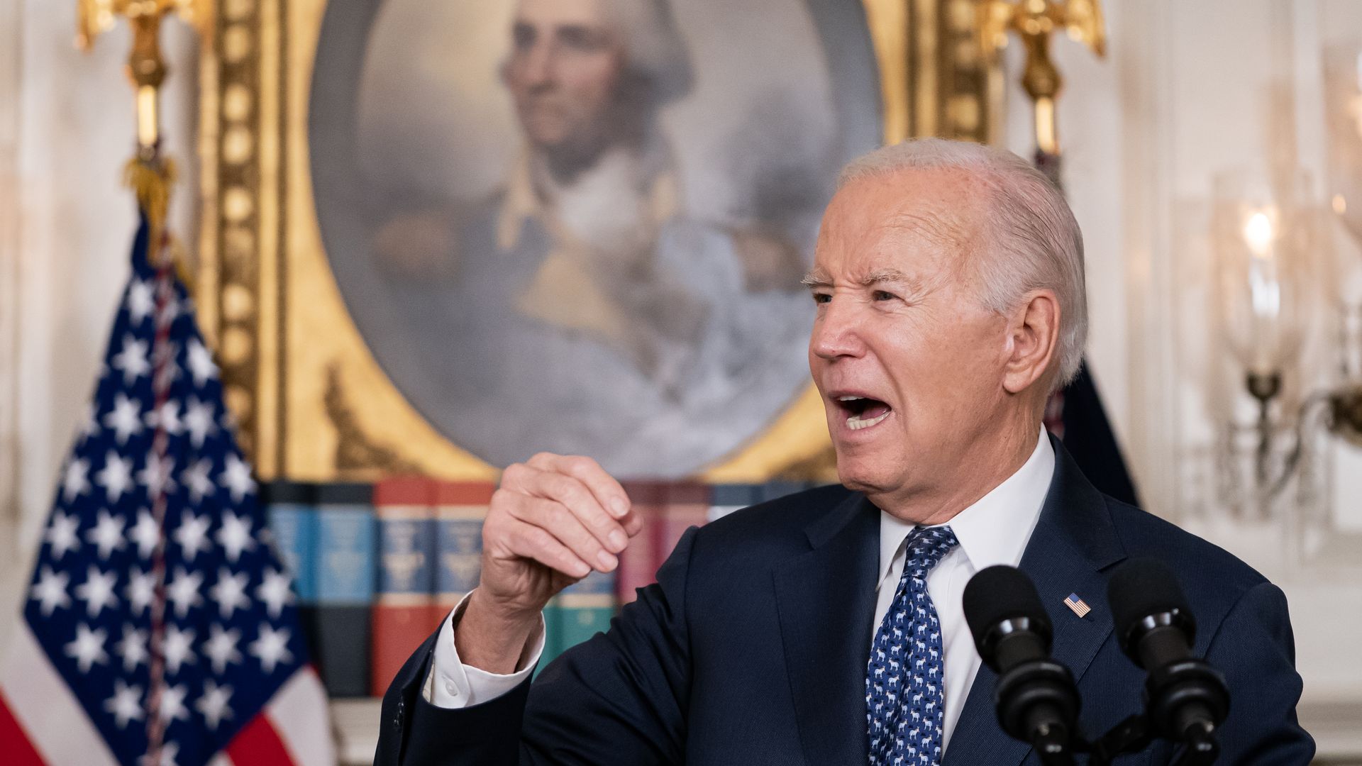 President Biden speaks behind a podium with a portrait of George Washington in the background.