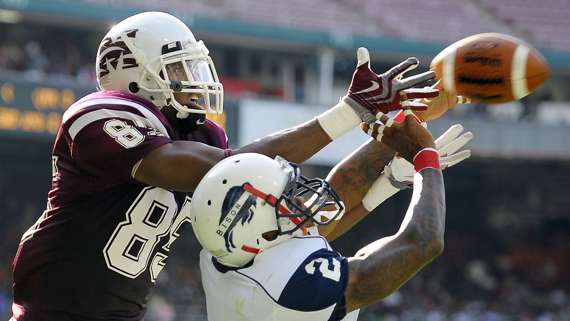 Two football players go up to catch a pass.