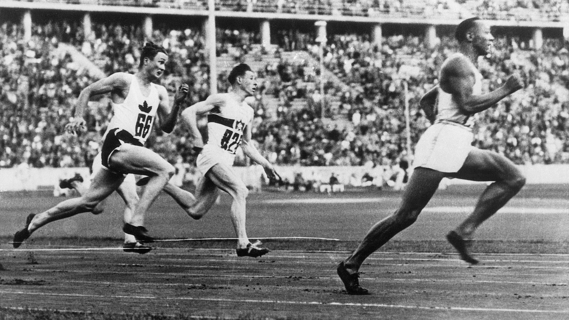 Jesse Owens and two other sprinters are seen running at the 1936 Olympic games. Owens is out in front of them. 