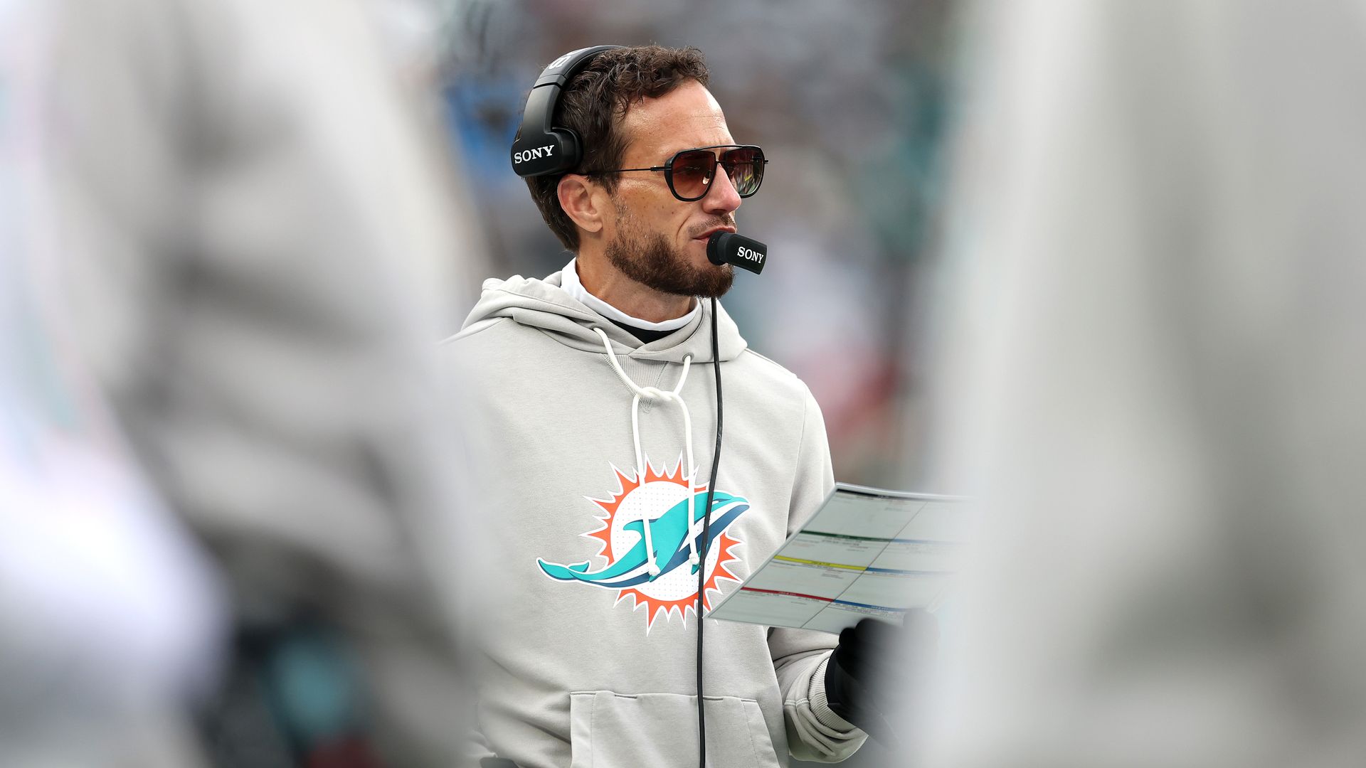 A football coach holding play cards and talking into his head set. 