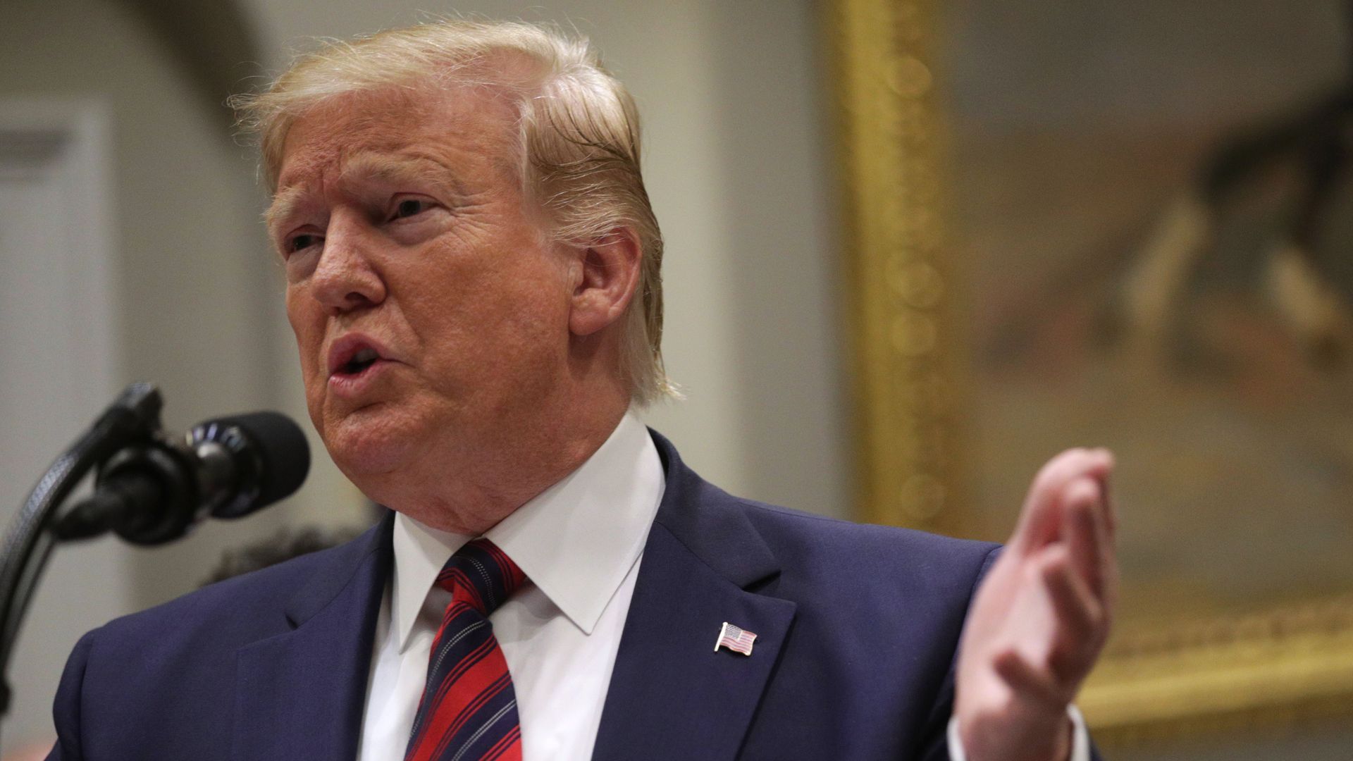 In this image, Trump speaks and gestures into a microphone.