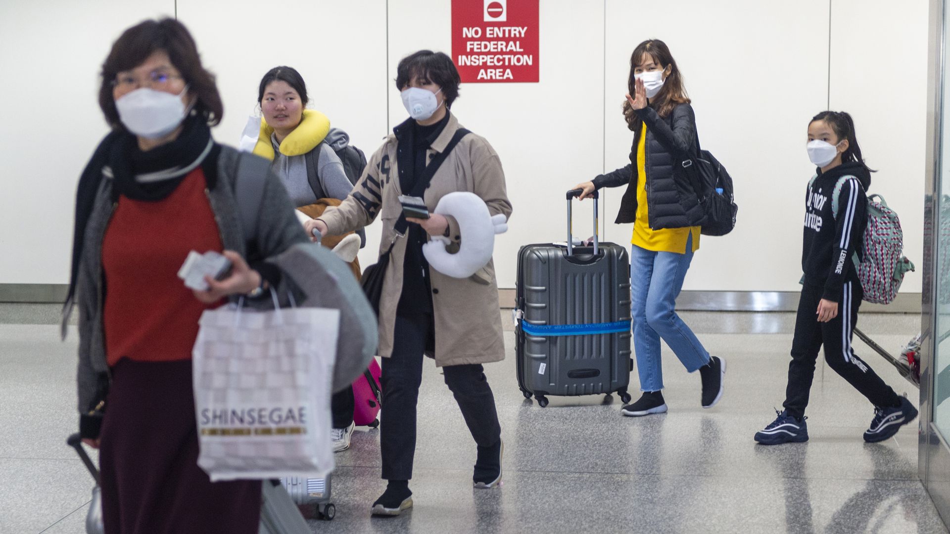 Airline passengers wearing face masks walk out of the international terminal at the San Francisco International Airport in Millbrae