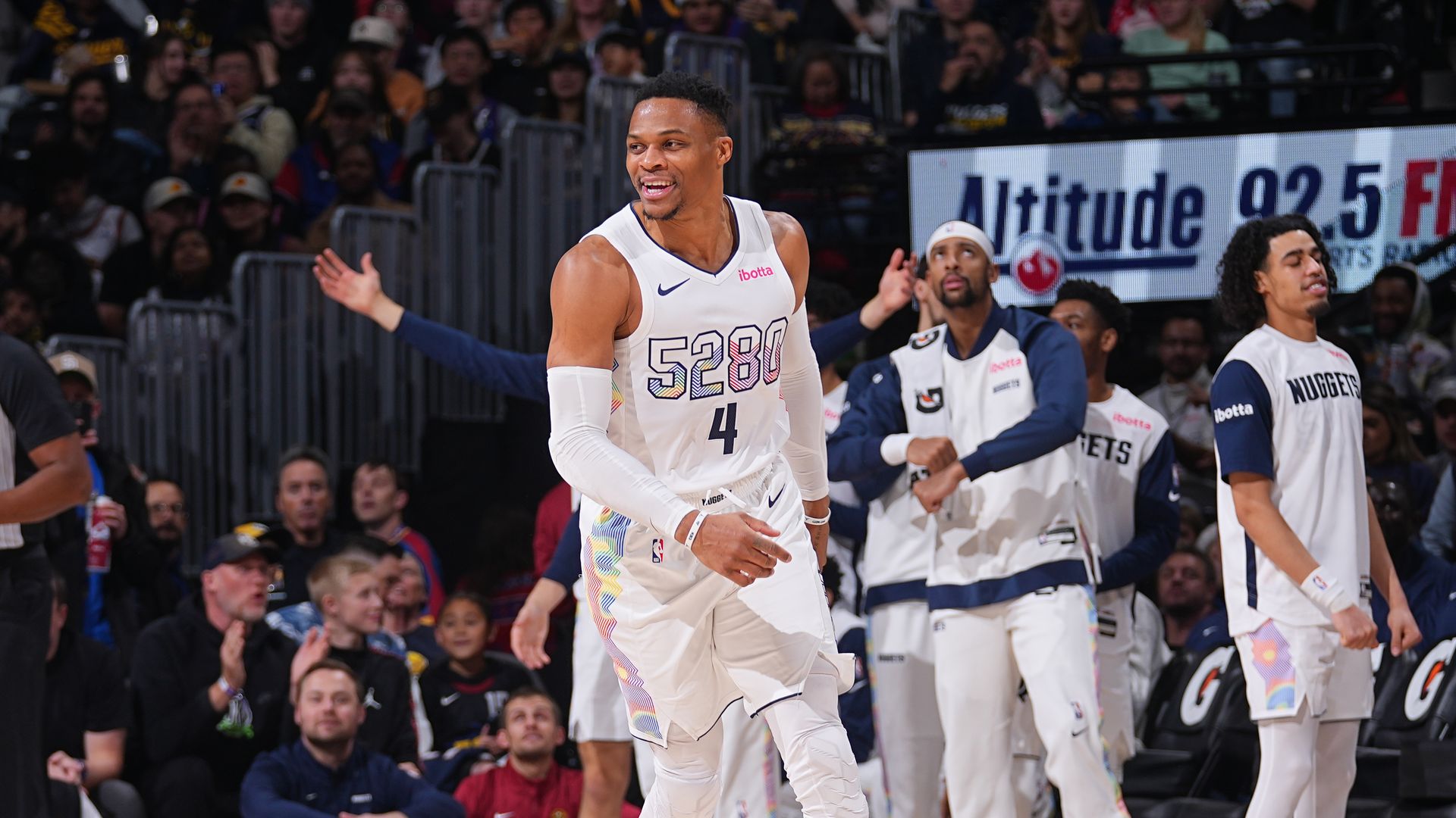 A man in a white jersey with the numbers 5280 and 4 smiles while looking on. 