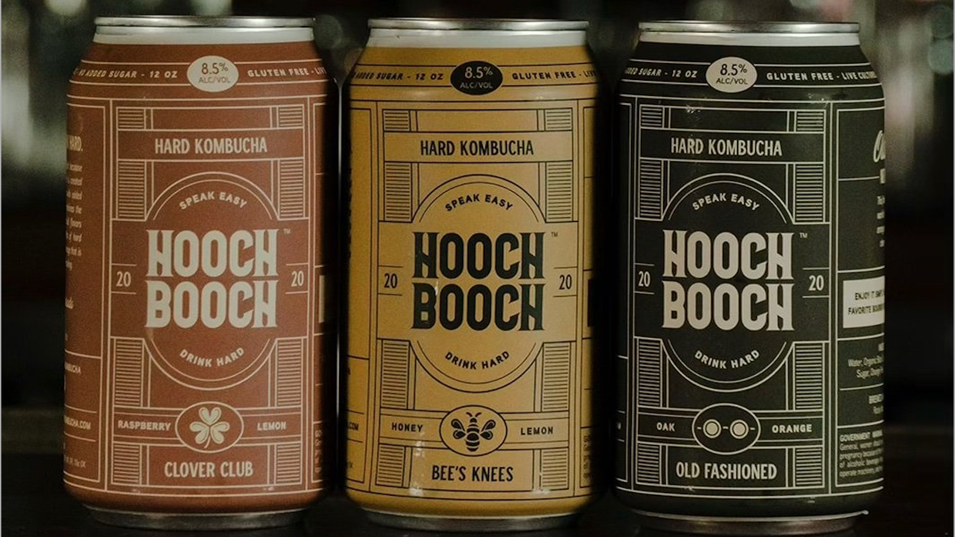 Three cans of hard kombucha side by side on a wooden table.