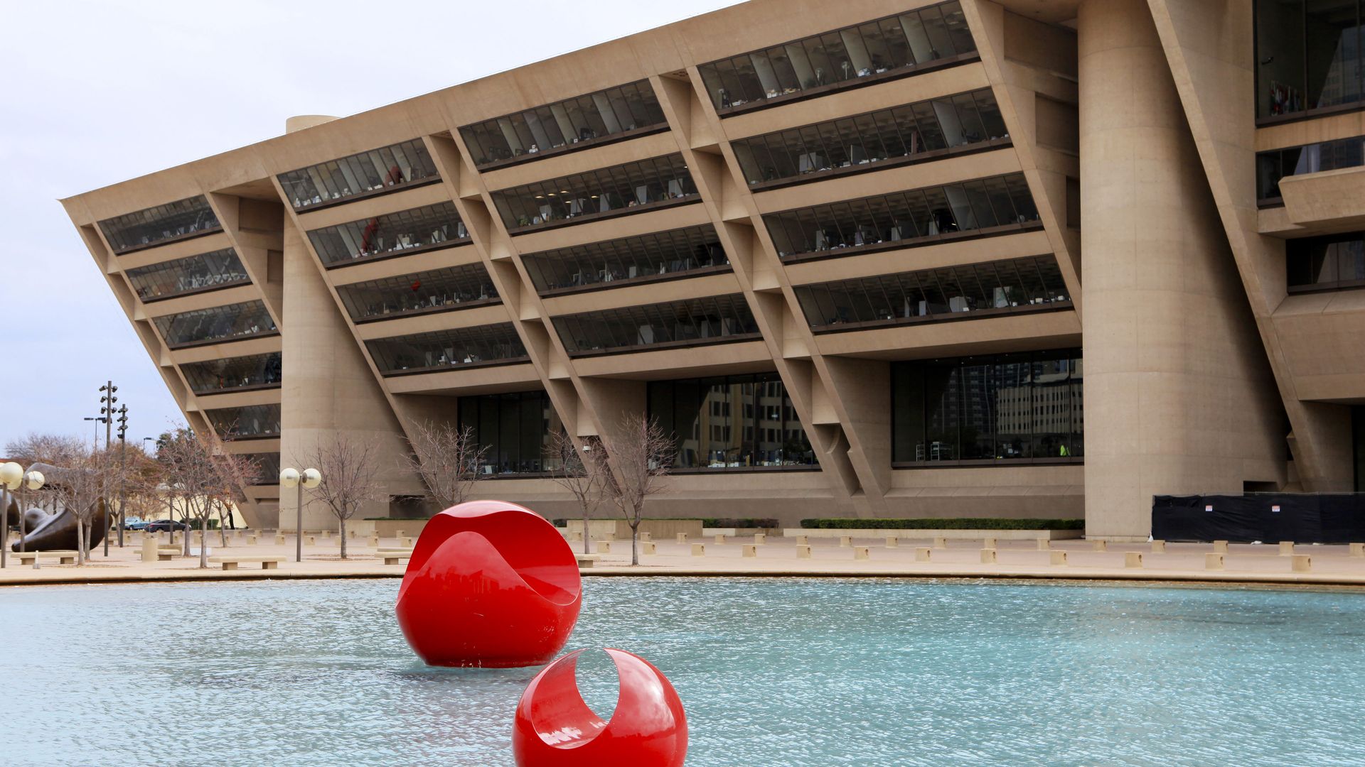 Two large red abstract sculptures are floating in a pool outside Dallas City Hall, an angular, brutalist design by renowned architect I.M. Pei. 