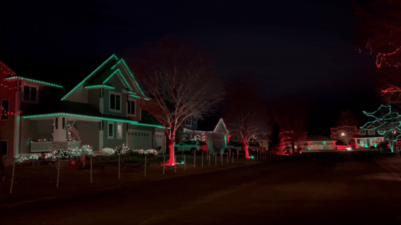 An animated image of a suburban cul-de-sac with a coordinated holiday light show strung along short poles and through the trees in several yards