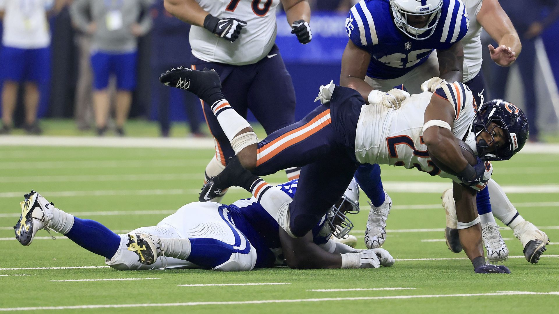 Chicago Bears player dives with the ball cradled in his right arm at an Indianapolis Colts player is on the ground.