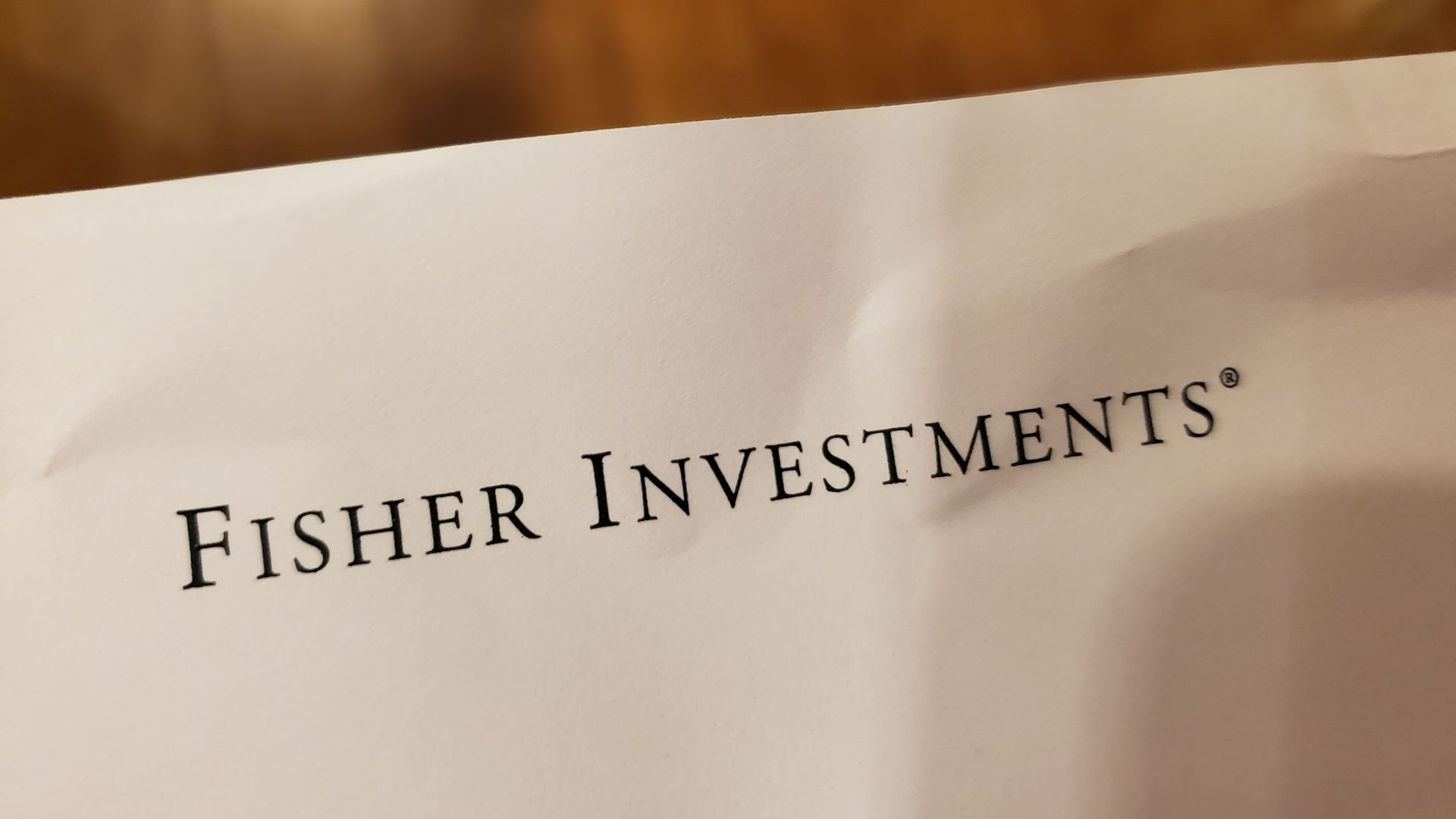 Close-up of logo for financial management company Fisher Investments on paper on light wooden background.