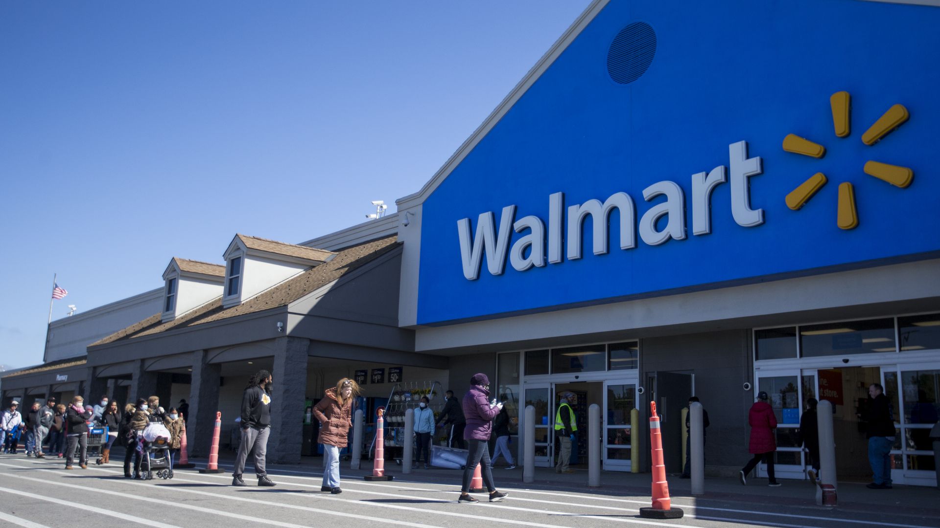 Picture of a Walmart store front with people waiting in line to go inside.