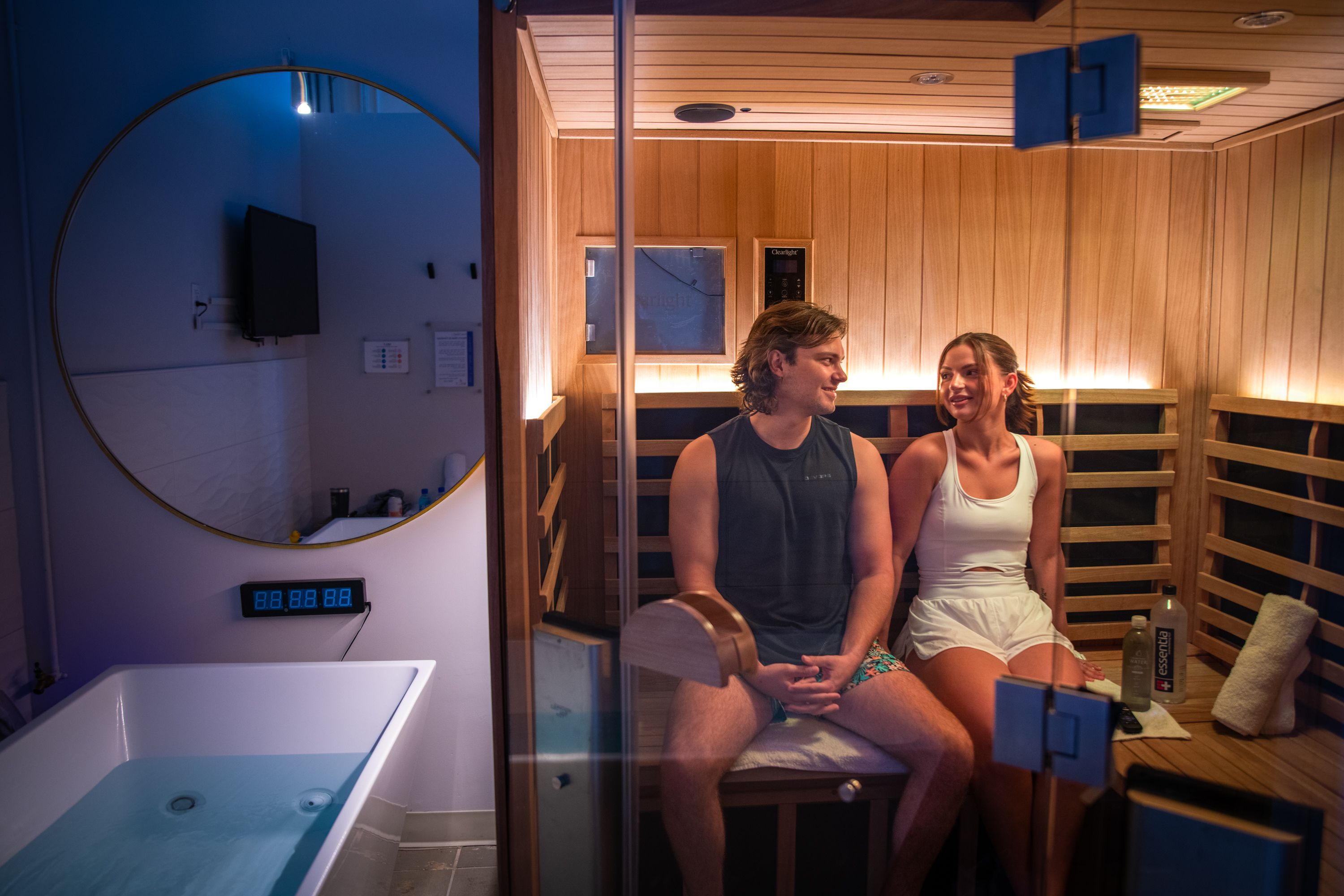 Photo shows two people inside a sauna with a cold plunge next to them.