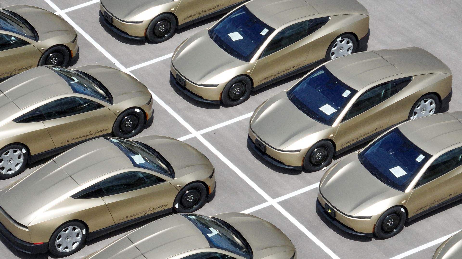 Overhead photo of two rows of gold Tesla Cybercabs parked nose to nose in a parking lot, with each parking space outlined in white paint.