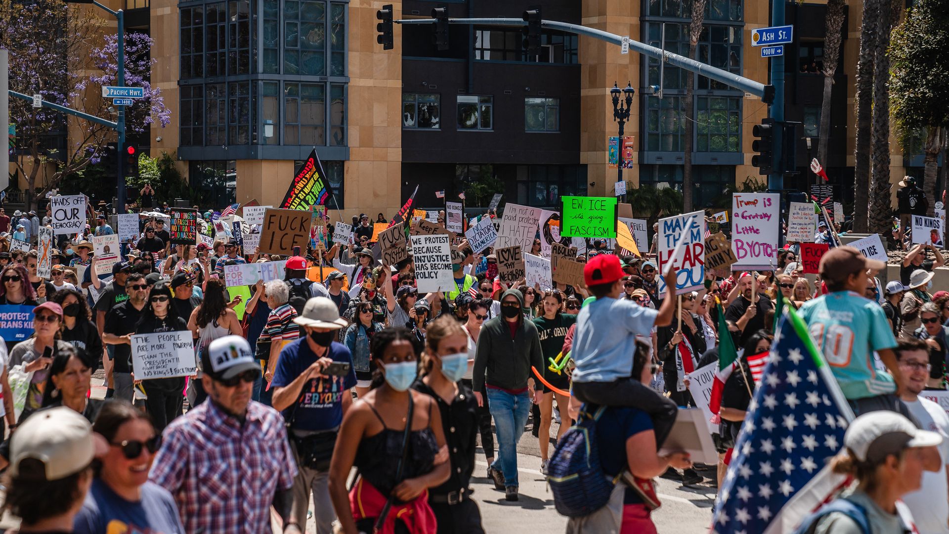 Hundreds of protesters walk down Pacific Highway in downtown San Diego carrying handmade signs and American flags.