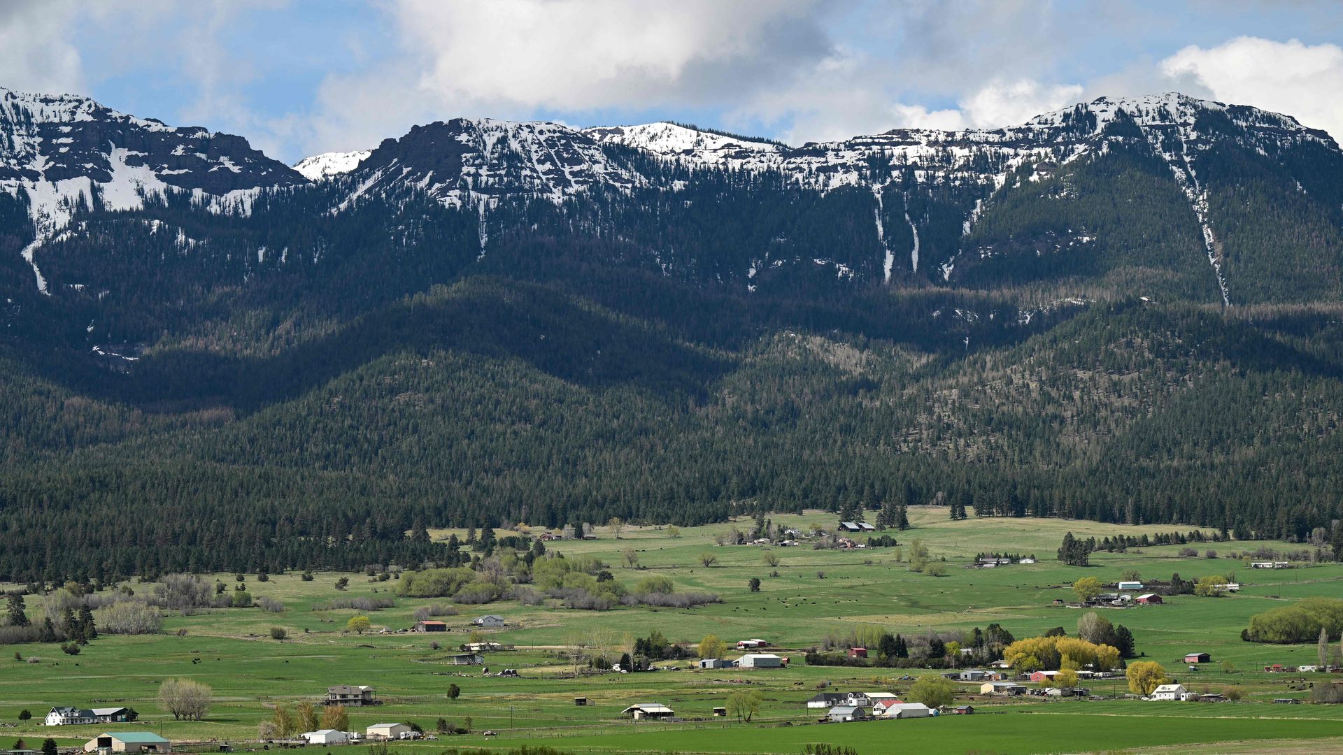 Tall mountains with snow on the top loom over a valley dotted with houses and farms.