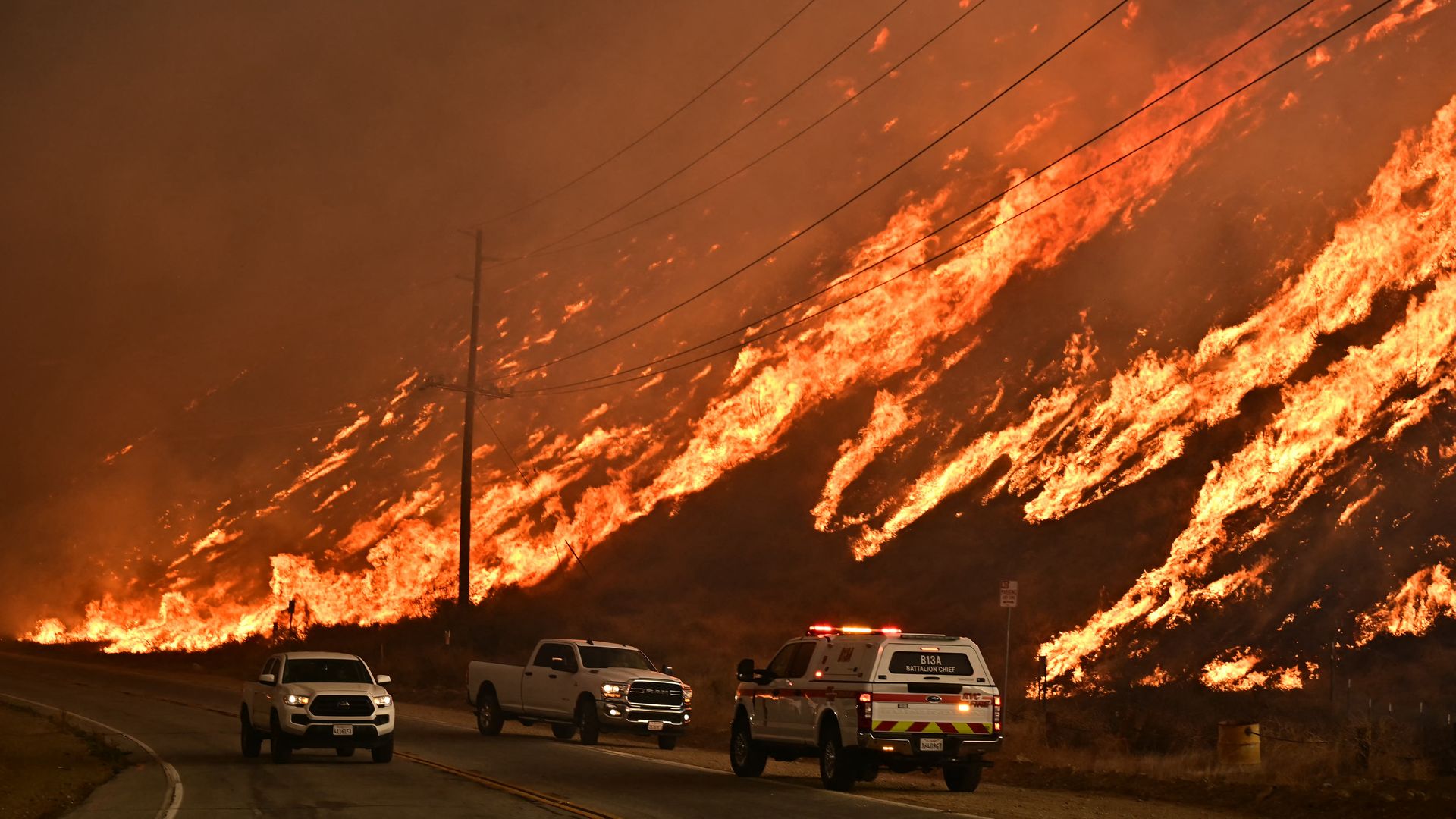 Emergency vehicles are parked next to a burning hillside in the LA area in January 2025 during a wildfire disaster.