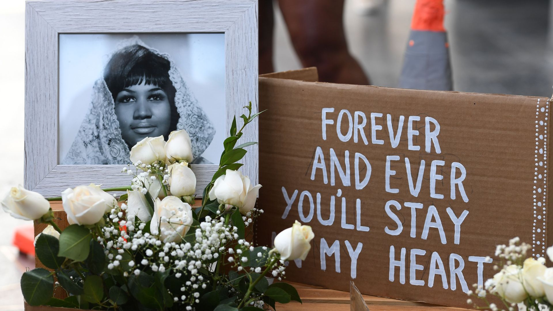 A photo of Aretha Franklin with flowers and a sign reading, "Forever you'll stay in my heart"